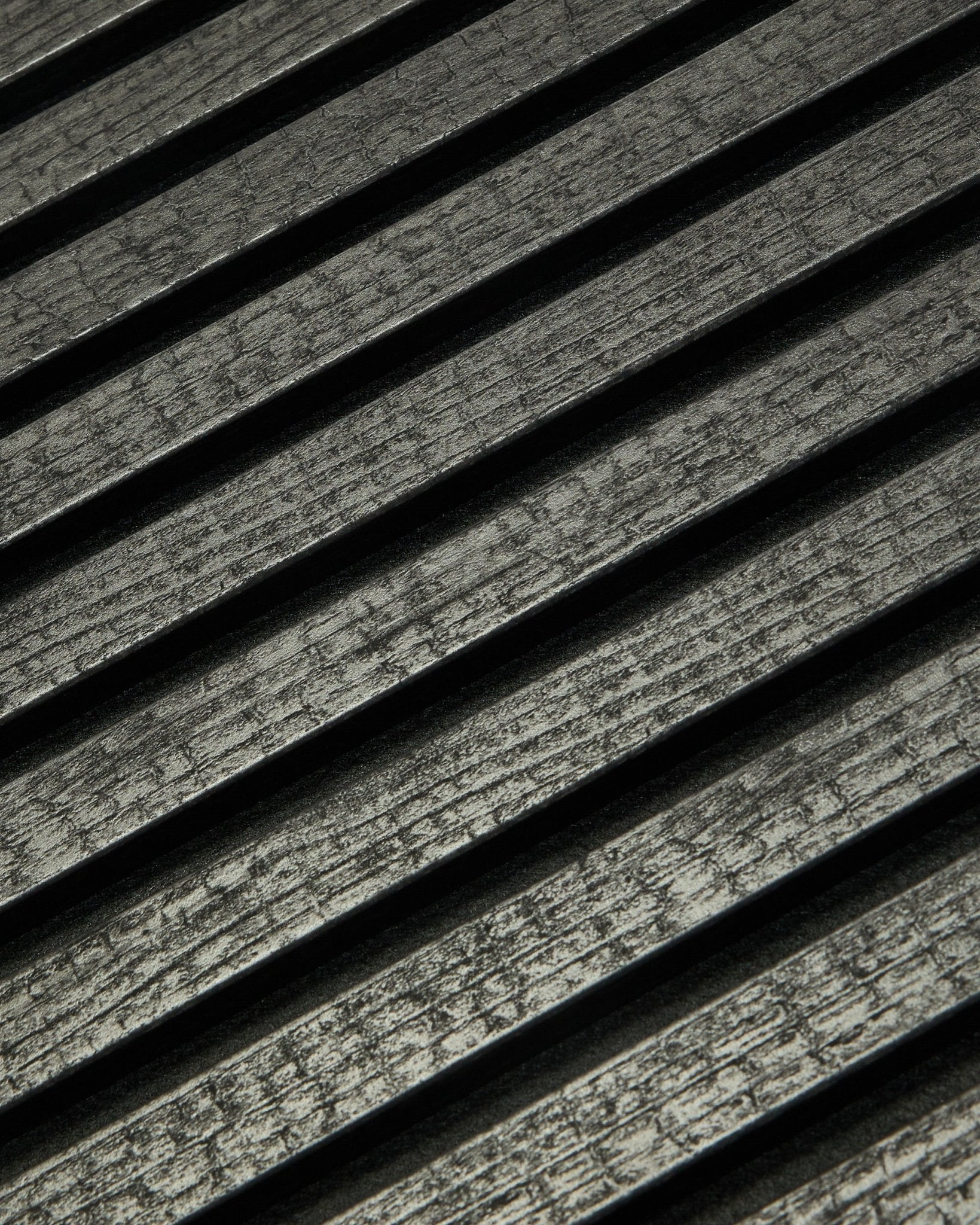 Gros plan sur le Akupanel Rebel de WoodUpp en Charcoal (240x60 cm), montrant des lattes acoustiques rainurées black disposées en diagonale pour une absorption acoustique renforcée.
