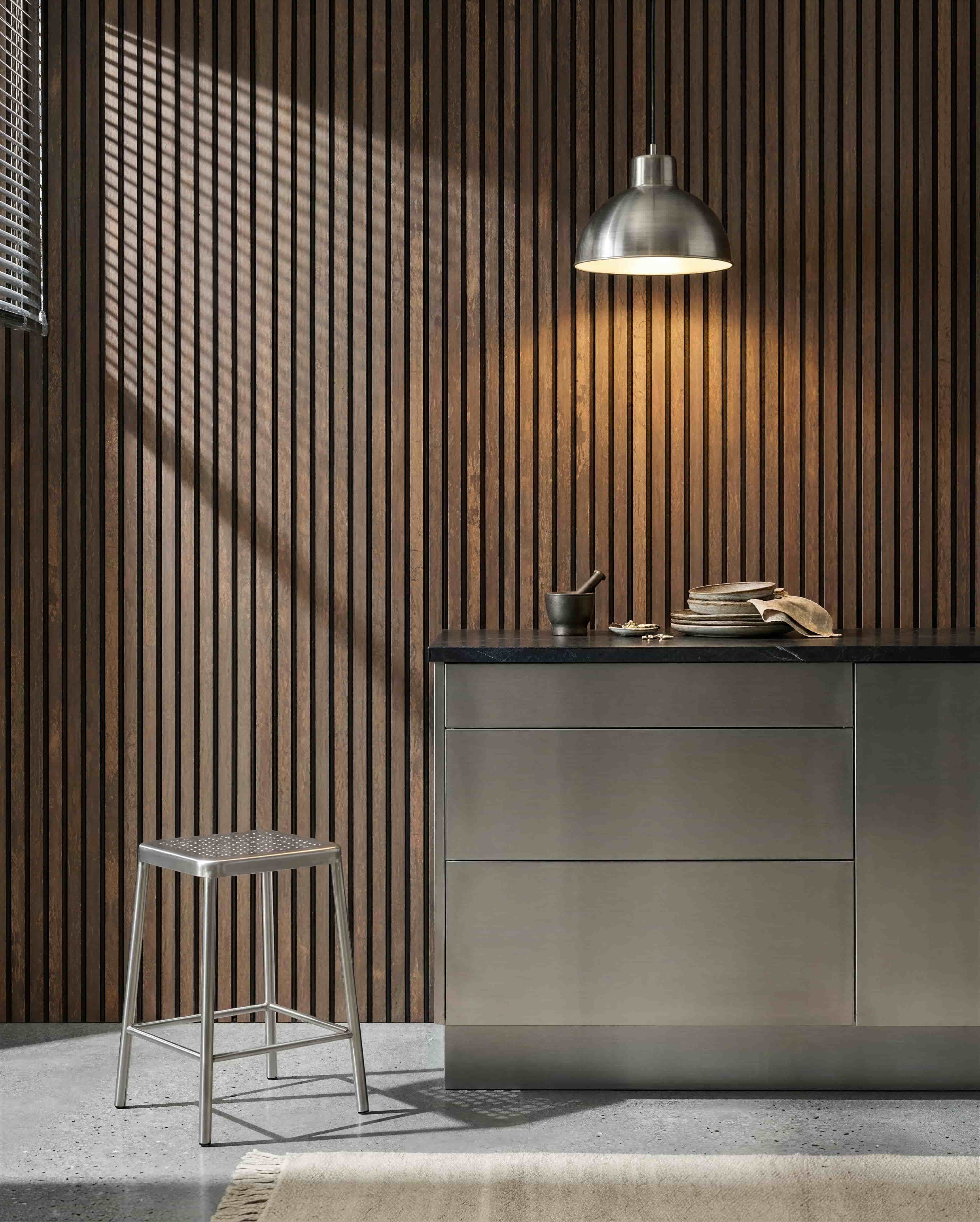 Cuisine avec un mur acoustique à lattes WoodUpp Akupanel Oxide Copper, un plan de travail en inox, un tabouret en métal, une suspension, de la vaisselle assortie et un mortier avec pilon.