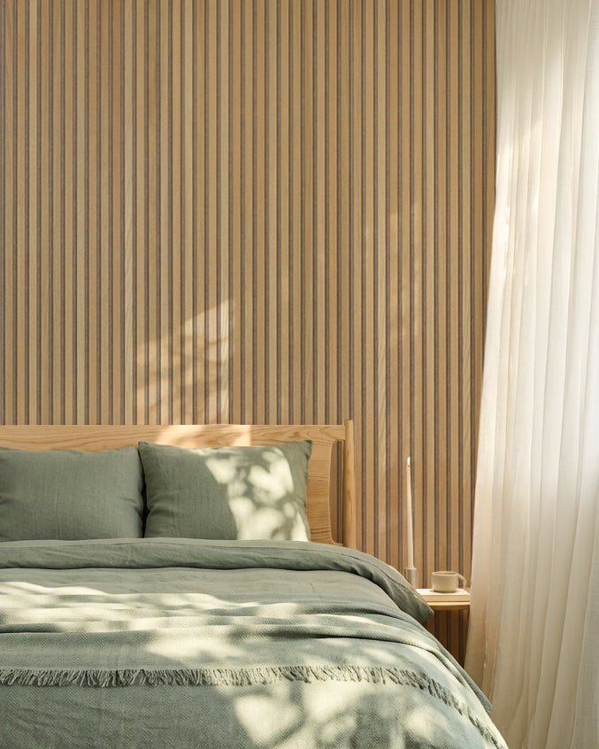 Chambre nordique minimaliste avec un mur en Panneau acoustique en chêne WoodUpp Akupanel, du linge de lit vert sauge, un cadre de lit en bois et des rideaux blancs vaporeux.