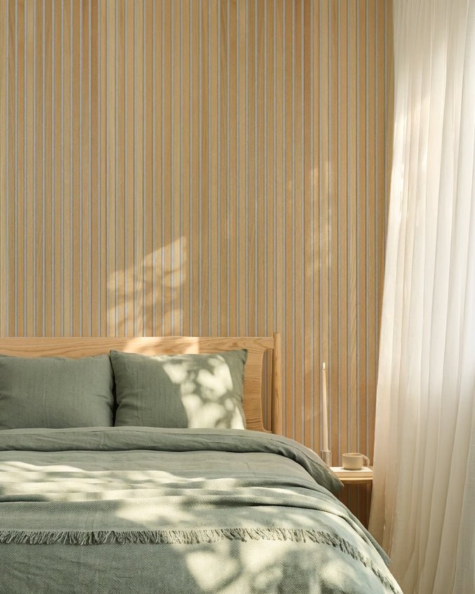 Minimalistisches nordisches Schlafzimmer mit salbeigrüner Bettwäsche und einer WoodUpp Classic Oak Akupanel Akustik-Lamellenwand; das Sonnenlicht erzeugt sanfte Schatten auf dem Bett.