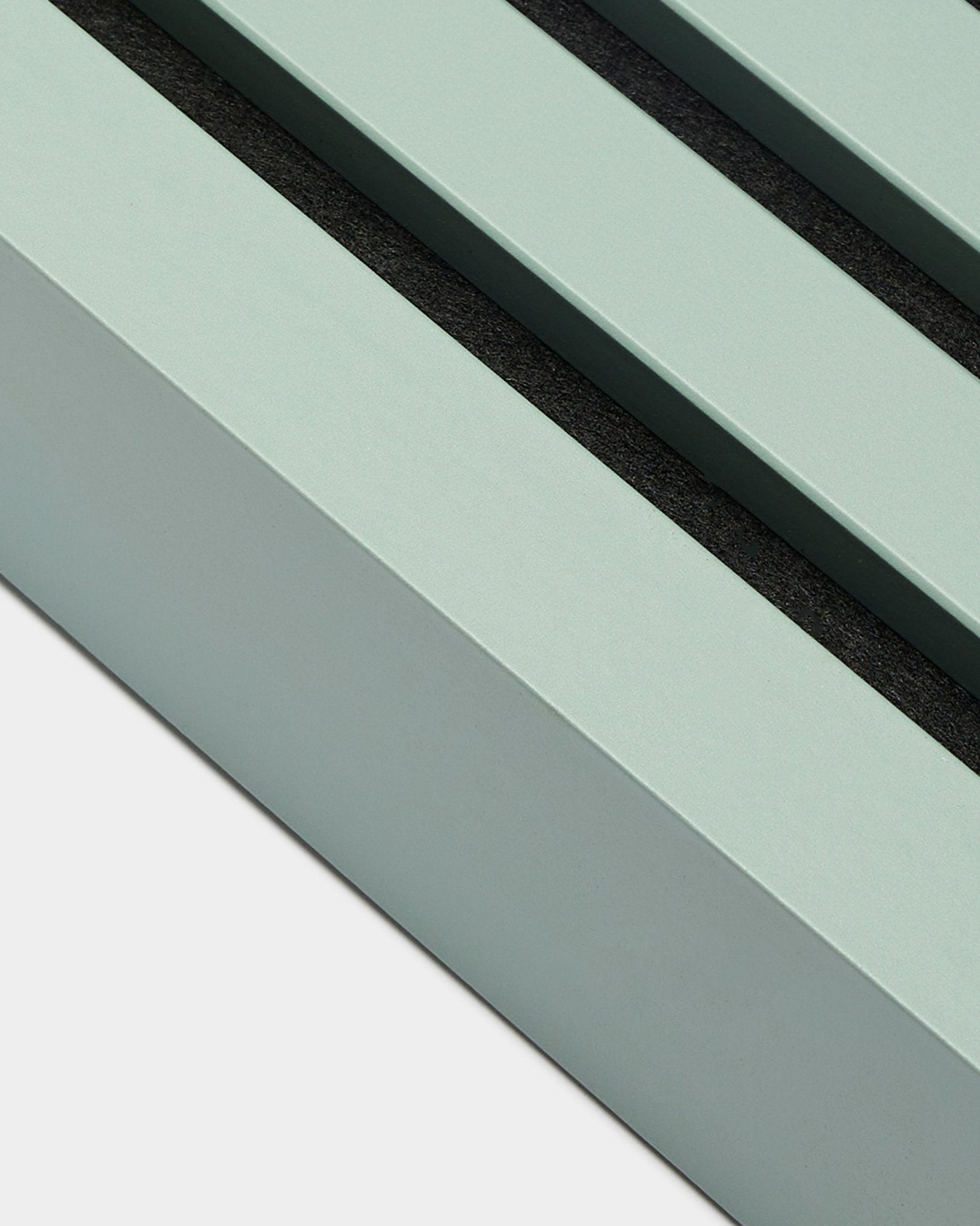 Gros plan sur l’accessoire d’installation WoodUpp Akupanel : lamelle de finition en Cloud, largeur 6,7 cm, cadre en MDF vert menthe avec deux rainures black sur fond blanc.