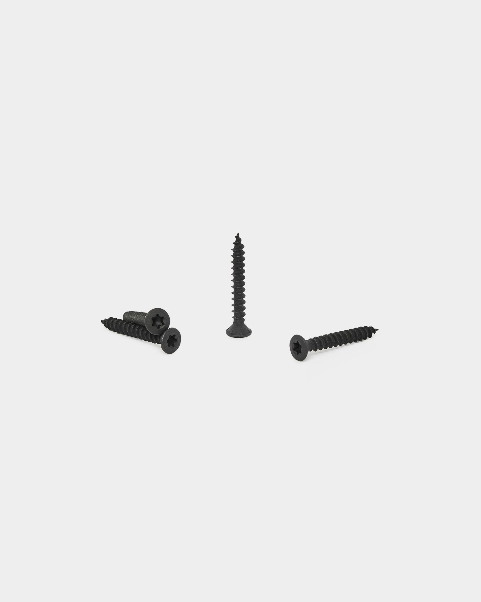 Quatre vis de pose WoodUpp black, trois à plat et une à la verticale, présentées sur fond blanc pour l’installation des Akupanel Panneau acoustique.
