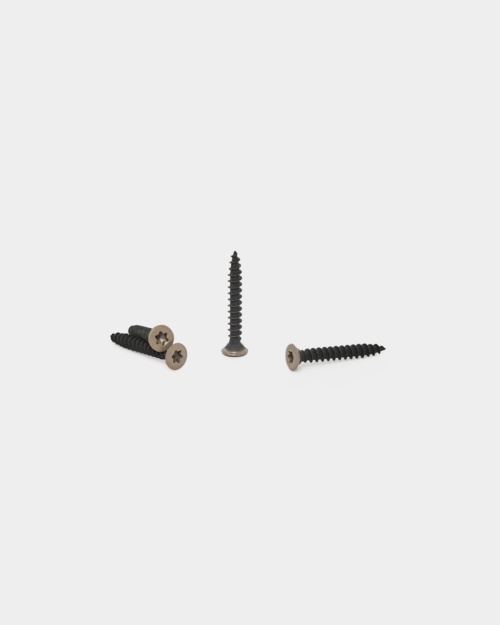 Trois vis warm grey pour les panneaux acoustiques WoodUpp sont disposées sur un fond blanc, une debout et deux à plat avec la tête visible.