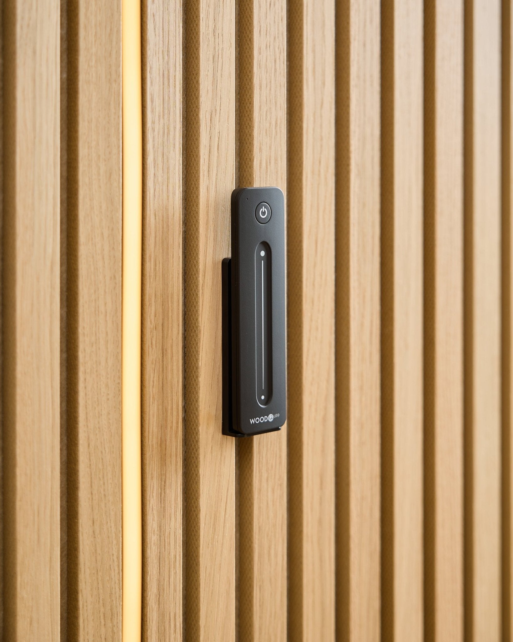 Un WoodUpp Lumi | Remote / LED Striplight est installé sur un panneau en bois clair Panneau acoustique, avec un câble jaune visible derrière les lattes en bois.