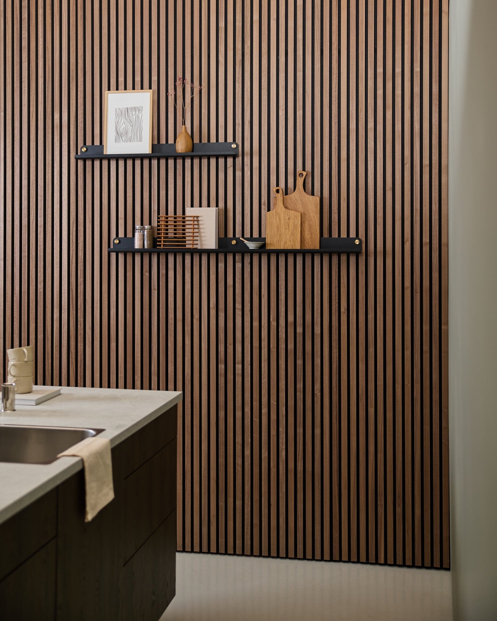 Cuisine moderne avec un panneau acoustique à lattes de style nordique, une étagère étroite WoodUpp black Norr (115,9 cm) pour la décoration, et une serviette posée sur l’évier.