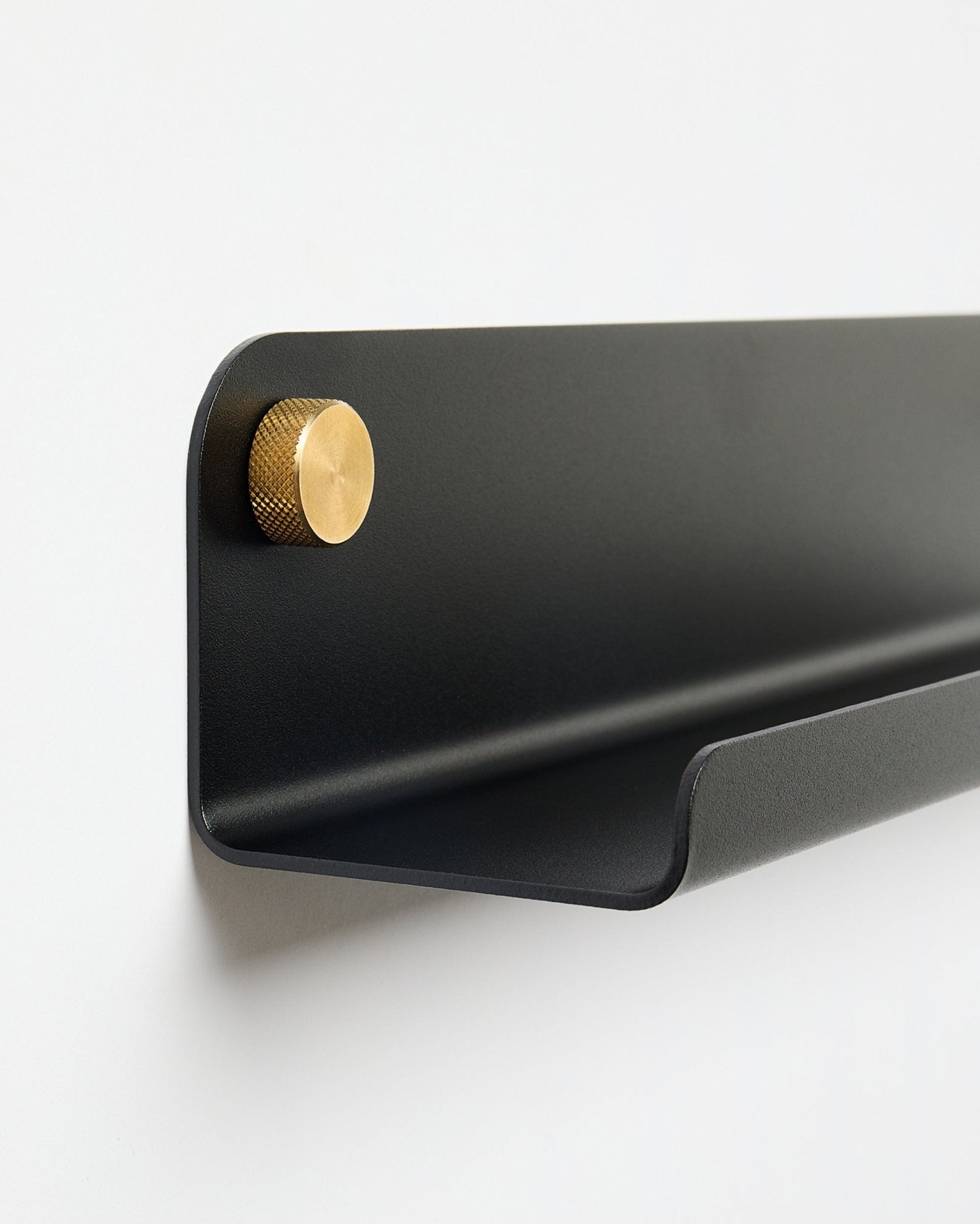 L’étagère | étroite Norr en black (115,9 cm) avec un unique bouton doré à gauche, par WoodUpp, fixée sur un mur blanc uni.
