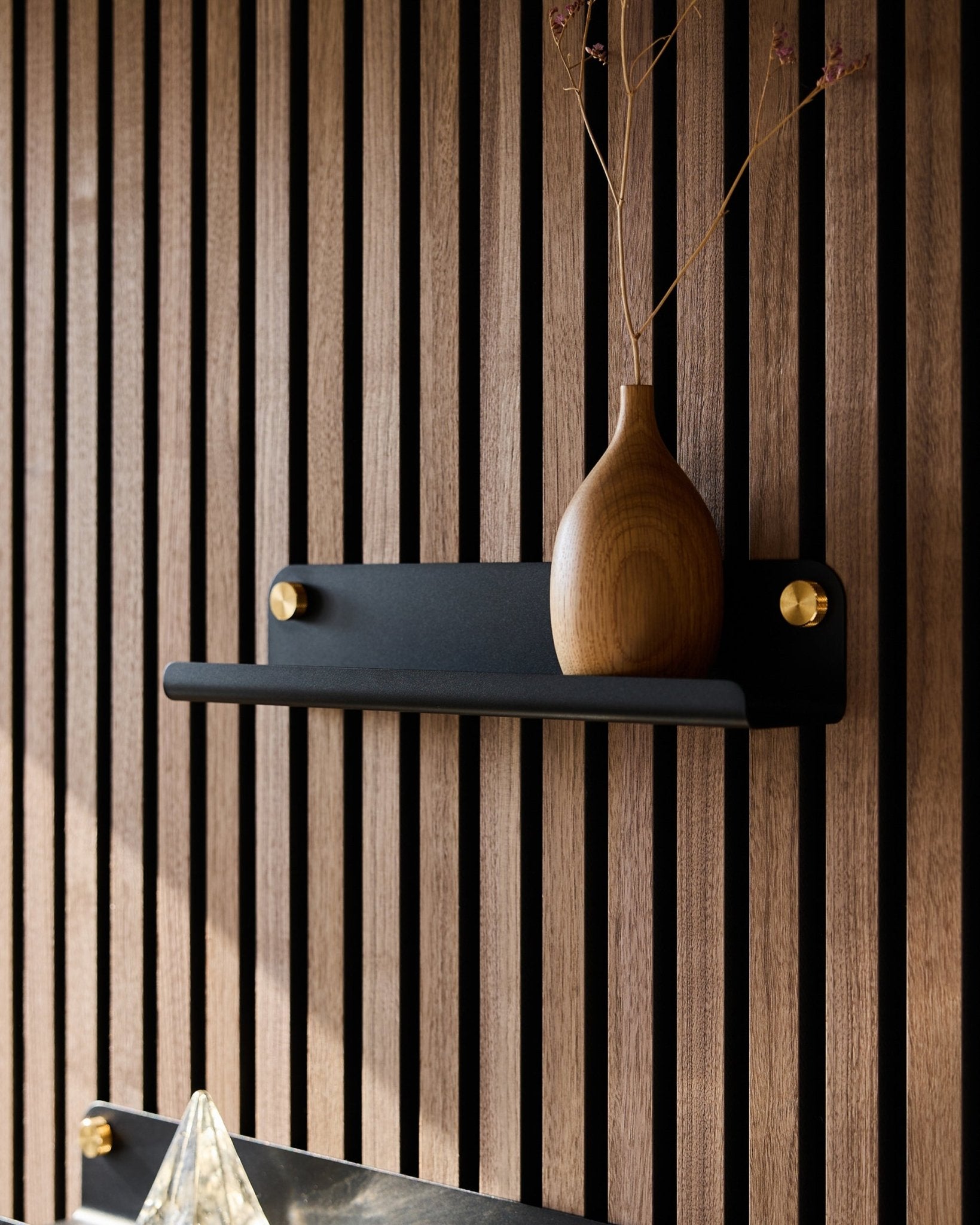 Un vase en bois avec des branches séchées sur une étagère étroite WoodUpp Norr Narrow Shelf (35,9 cm) en black, devant un panneau acoustique à lattes de style nordique vertical.