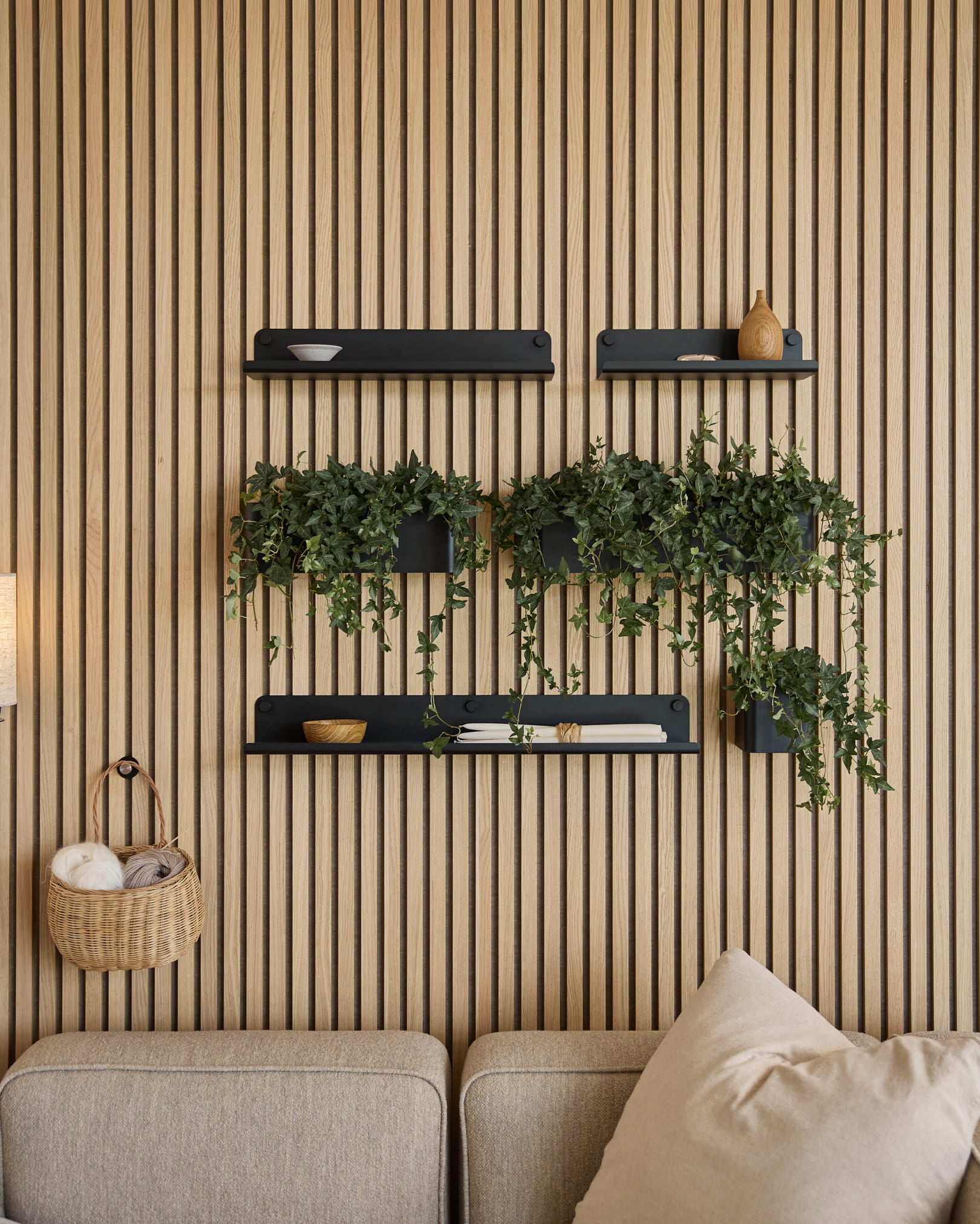 Salon moderne avec un panneau mural acoustique nordique à lattes, des étagères black, des plantes retombantes dans le Norr Plant Box de WoodUpp (35,9 cm, Black), et un canapé beige.