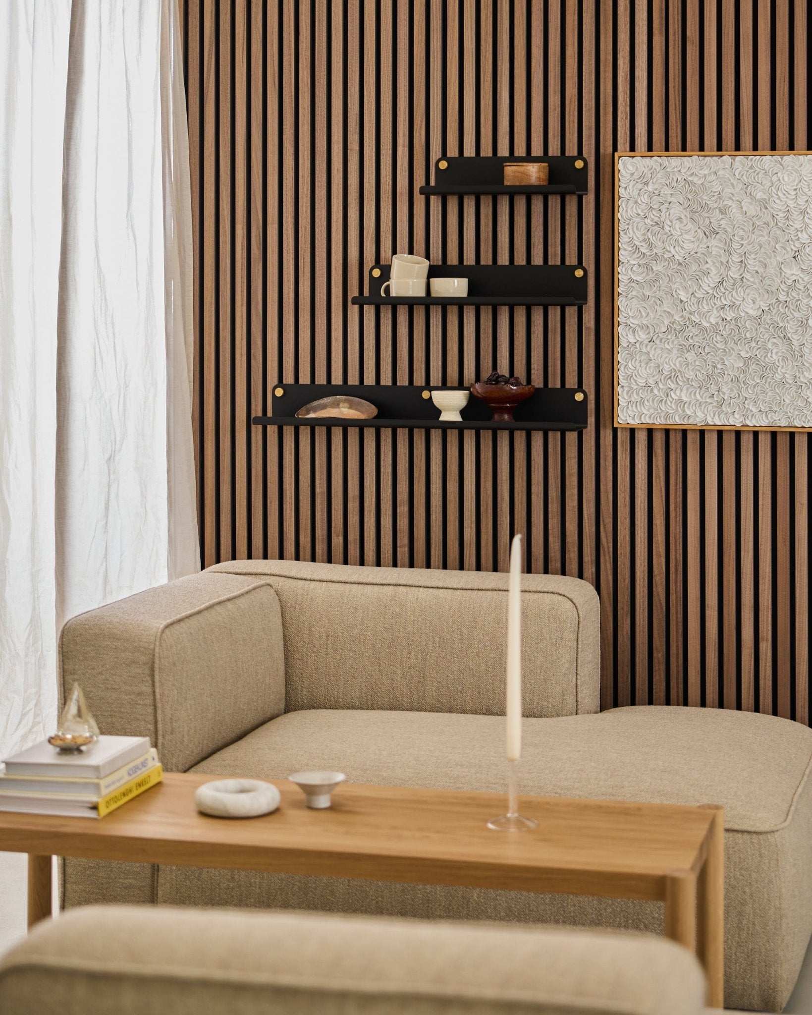 Salon moderne avec un canapé beige, une table en bois, une étagère large WoodUpp black Norr (51,9 cm) et un mur en Akupanel Panneau acoustique texturé, agrémenté d’une œuvre abstraite.