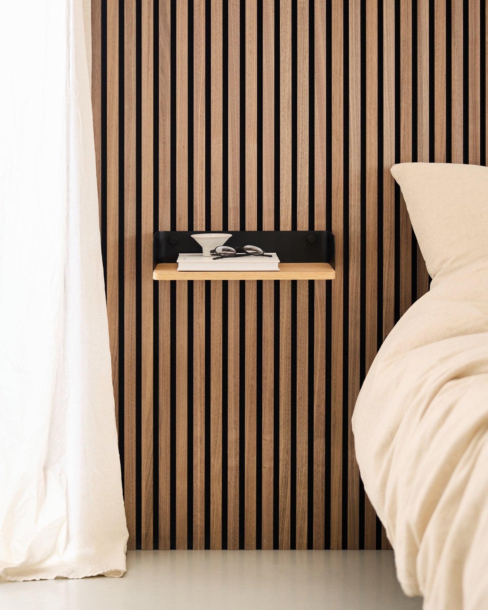 Chambre minimaliste avec un mur en Panneau acoustique à lattes de bois nordique, la bibliothèque WoodUpp Linn en Natural Oak, et une table de chevet suspendue à côté d’un lit beige.