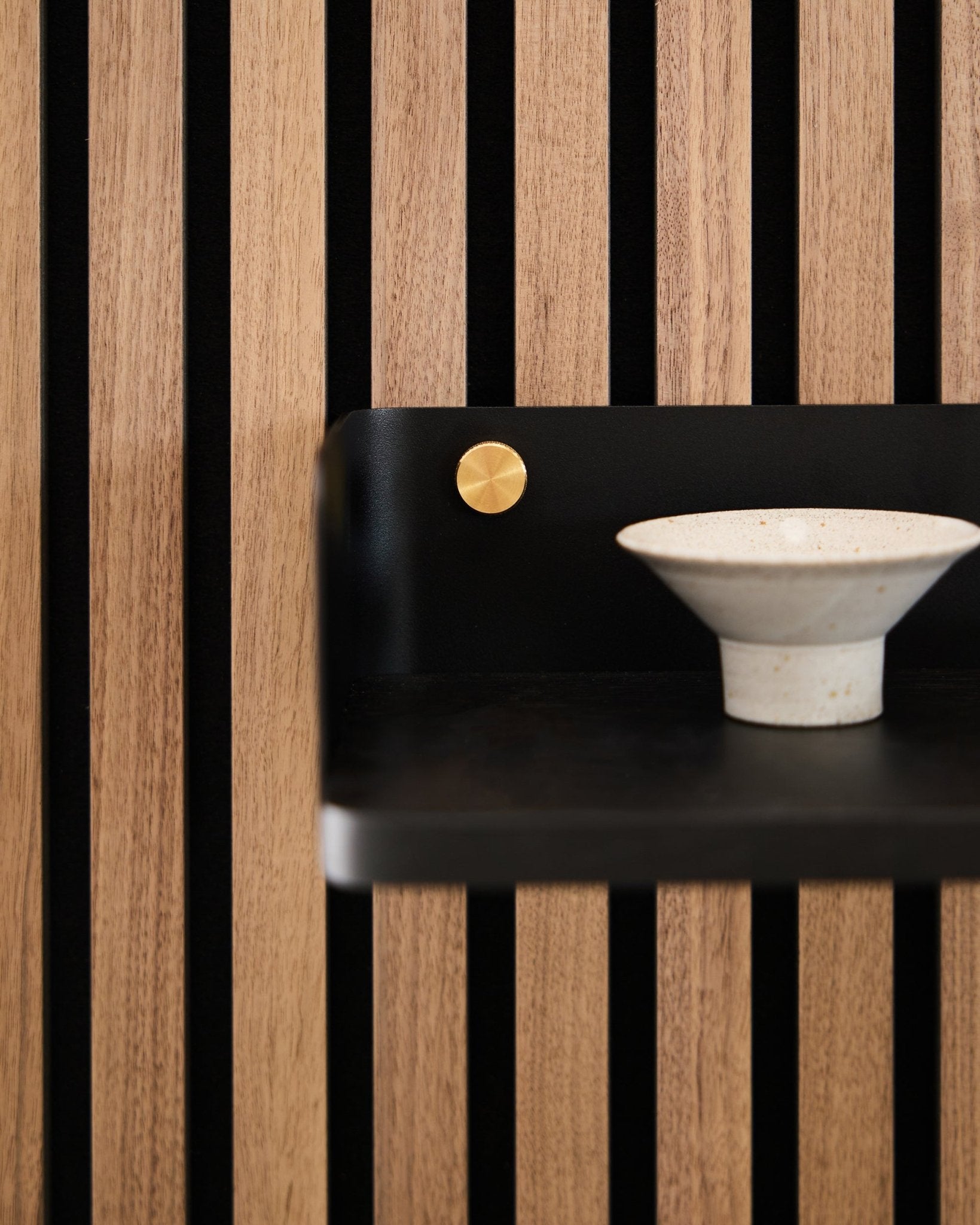 Bol en céramique posé sur l’étagère Linn de WoodUpp, 39,9 cm en black oak avec des lattes vertical black et une touche de brass, dans un esprit minimaliste nordique.