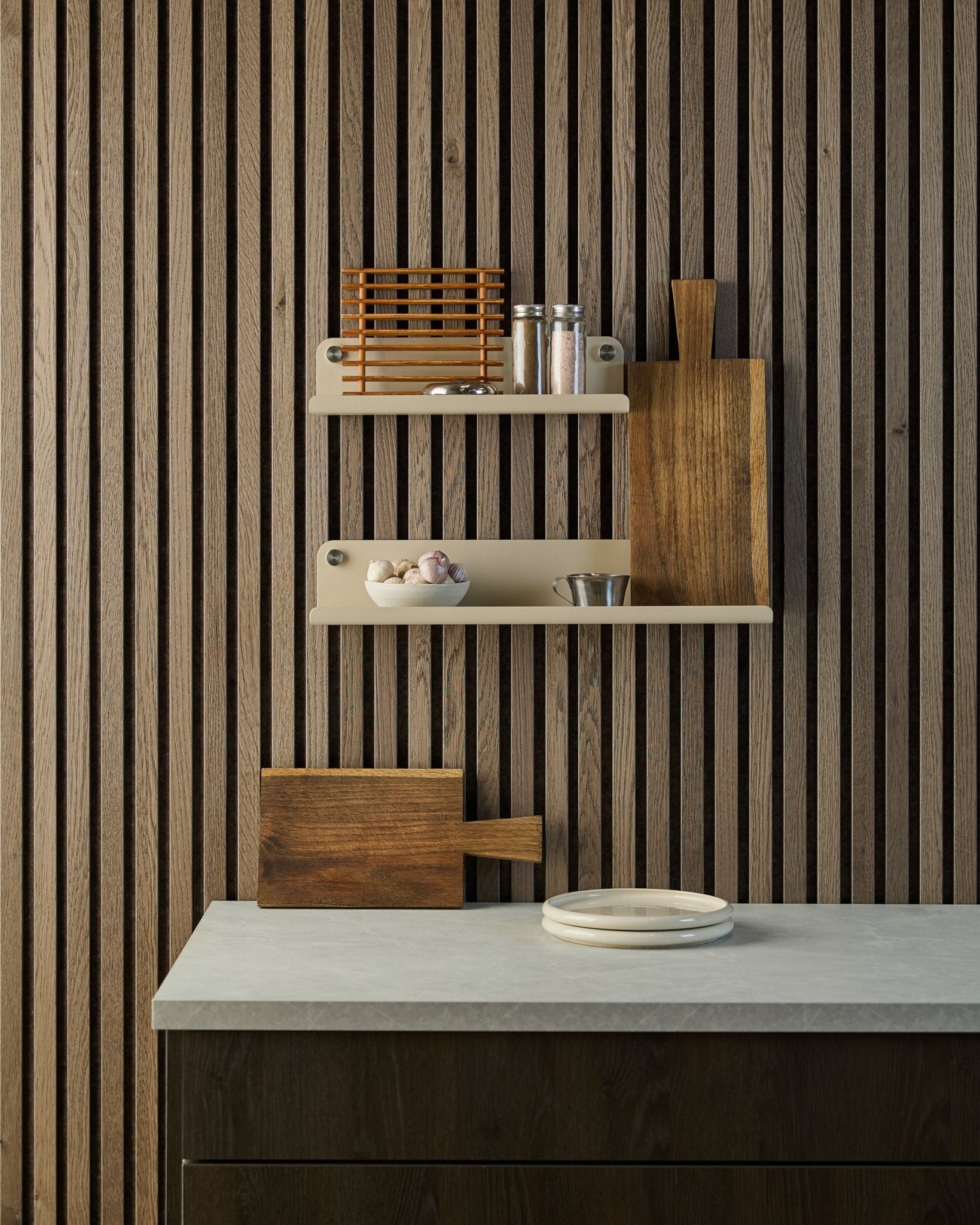 Cuisine minimaliste avec mur en lattes acoustiques en bois Akupanel de style nordique, étagères ouvertes avec épices et bols, plan de travail avec assiettes blanches et planche à découper.