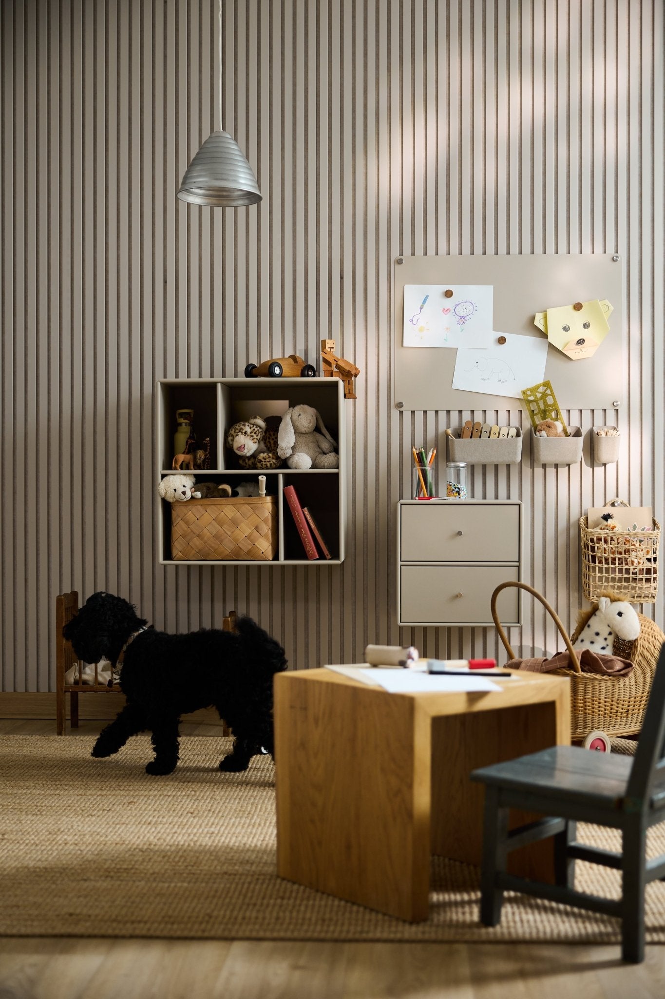 Salle de jeux avec un chien noir, des meubles danois, des jouets, du matériel de loisirs créatifs, des dessins denfants, de la lumière naturelle et une armoire ouverte WoodUpp Arka.