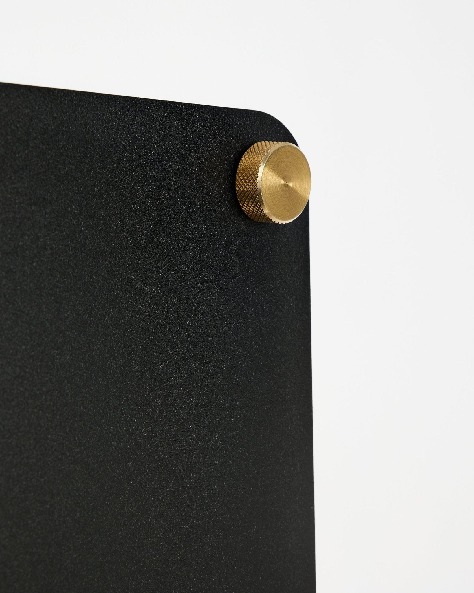 Nahaufnahme der WoodUpp Norr Akustik-Magnettafel in black (small) mit abgerundeter Ecke und goldener Schraubbefestigung vor weißem Hintergrund.