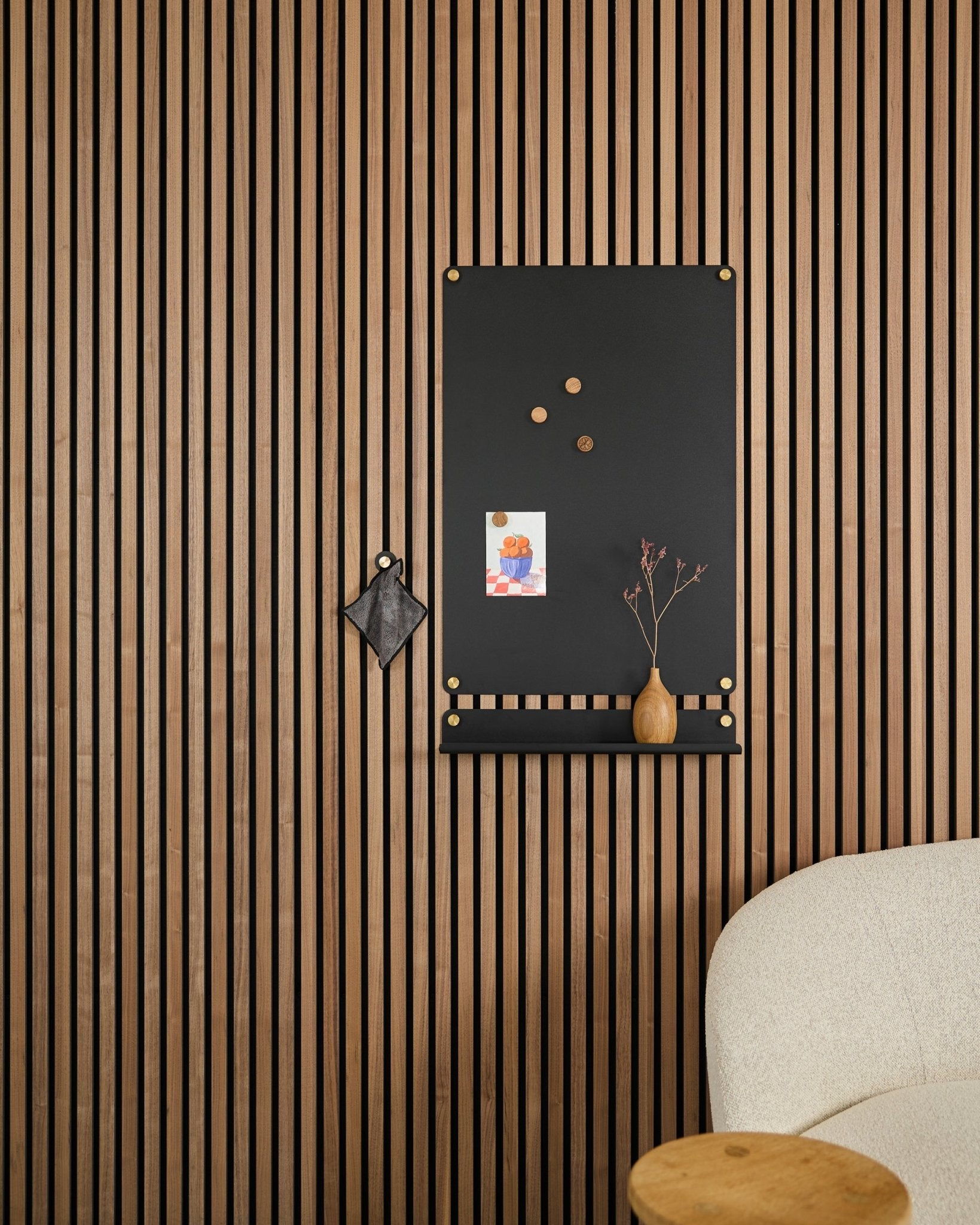 Eine large black Norr Magnettafel von WoodUpp, entworfen für Akustikpaneele, hängt neben einem weißen Polsterstuhl mit Notizen, einer Vase und einem kleinen Deko-Objekt.