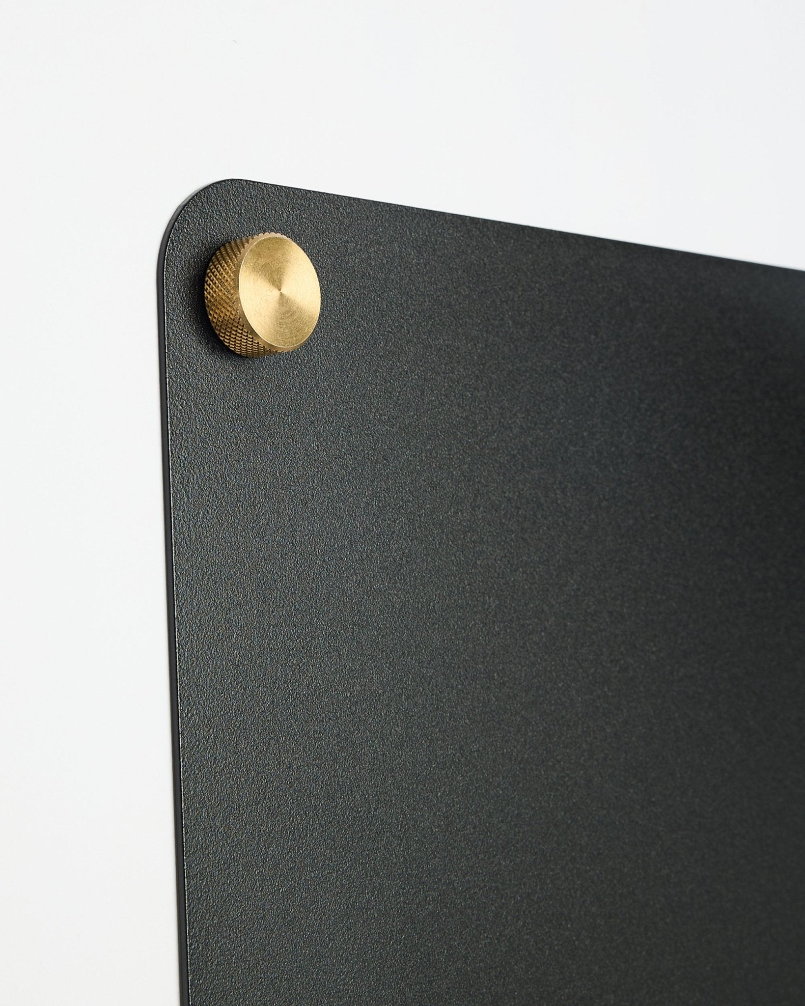 Nahaufnahme einer large black Norr Magnettafel von WoodUpp aus der CREATE Kollektion mit einem runden gold-coloreden Metallverschluss in der oberen Ecke.
