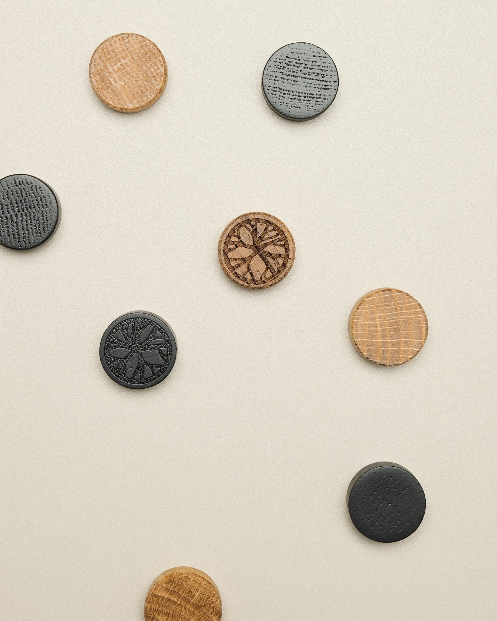 Das Norr Magnet-Set von WoodUpp umfasst vier Scheiben mit Muster in natural oak und black, ordentlich auf einer hellen beige Oberfläche platziert; ein Accessoire für Akupanel.