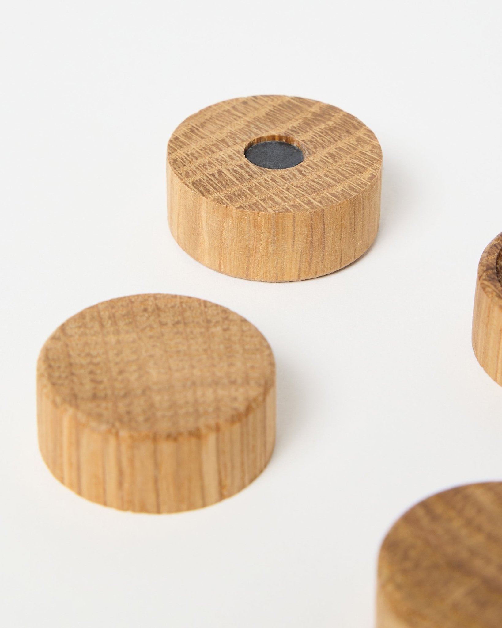 Set aus vier Magneten aus natural oak von WoodUpp, konzipiert für die Verwendung mit Akupanel Akustikholzpaneelen, einer davon mit zentralem Neodym-Magneten für extra Halt, auf Weiß präsentiert.