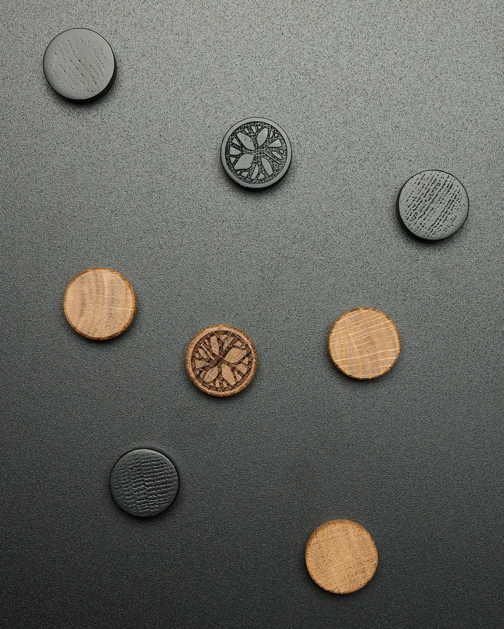 Vier runde black oak Magnete aus dem WoodUpp Norr Magnet-Set, locker auf einer dunkel strukturierten Oberfläche angeordnet, gestaltet als Zubehör für Akupanel.