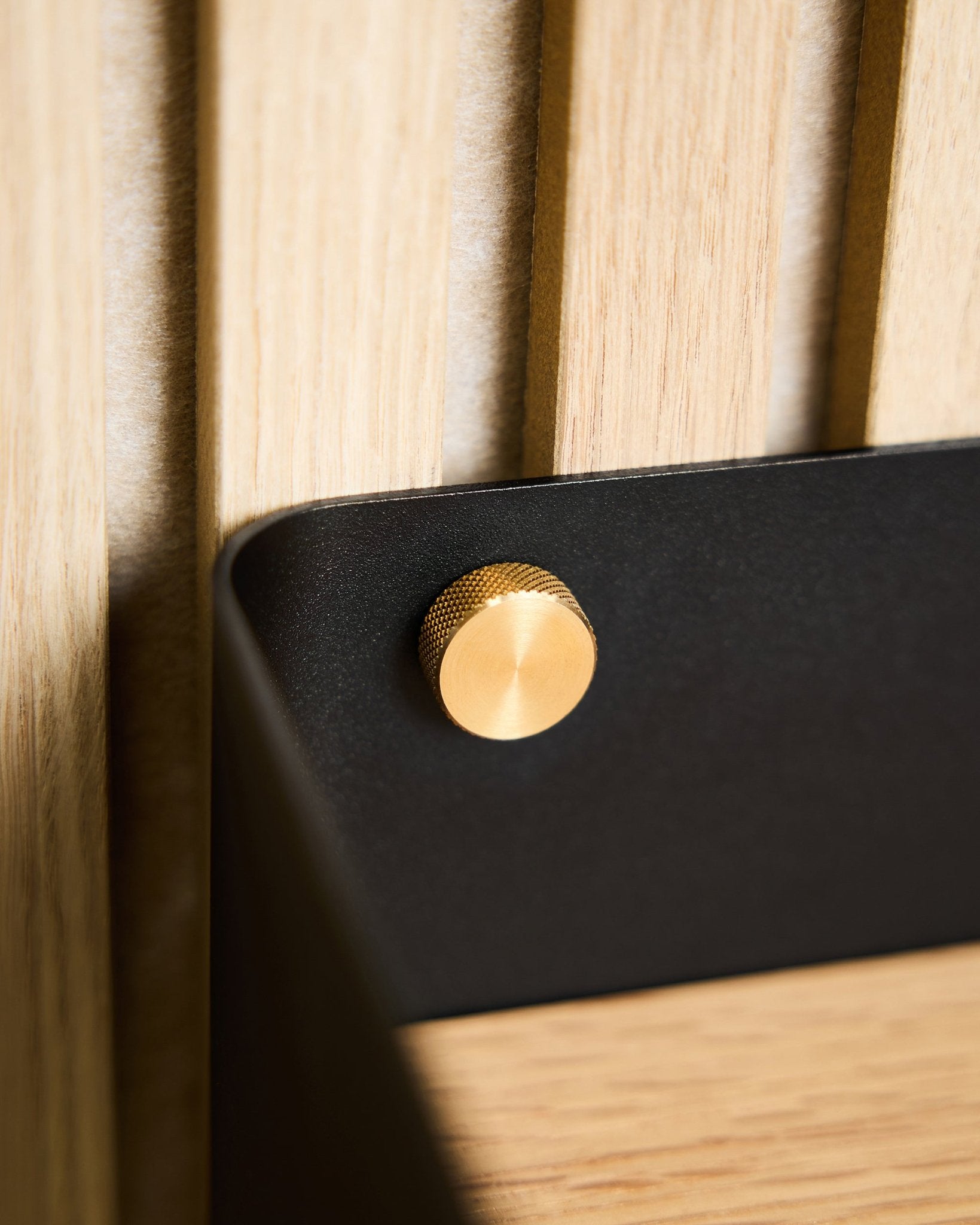 Nahaufnahme von zwei WoodUpp brass-Rändelschrauben (M5x10mm, 20x8.8), befestigt an einer black Halterung auf der Oberfläche eines hellen nordischen Holz-Akustikpaneels.