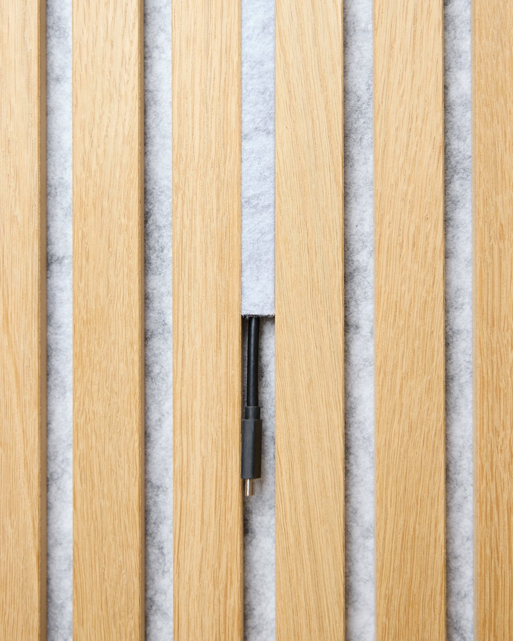 Das Dupps Pop-on-Kabelabdeckungsset (grey, 3 Stk.) von WoodUpp ordnet Kabel zwischen hellen Akupanel Lamellen vor einem weißen, strukturierten Hintergrund.
