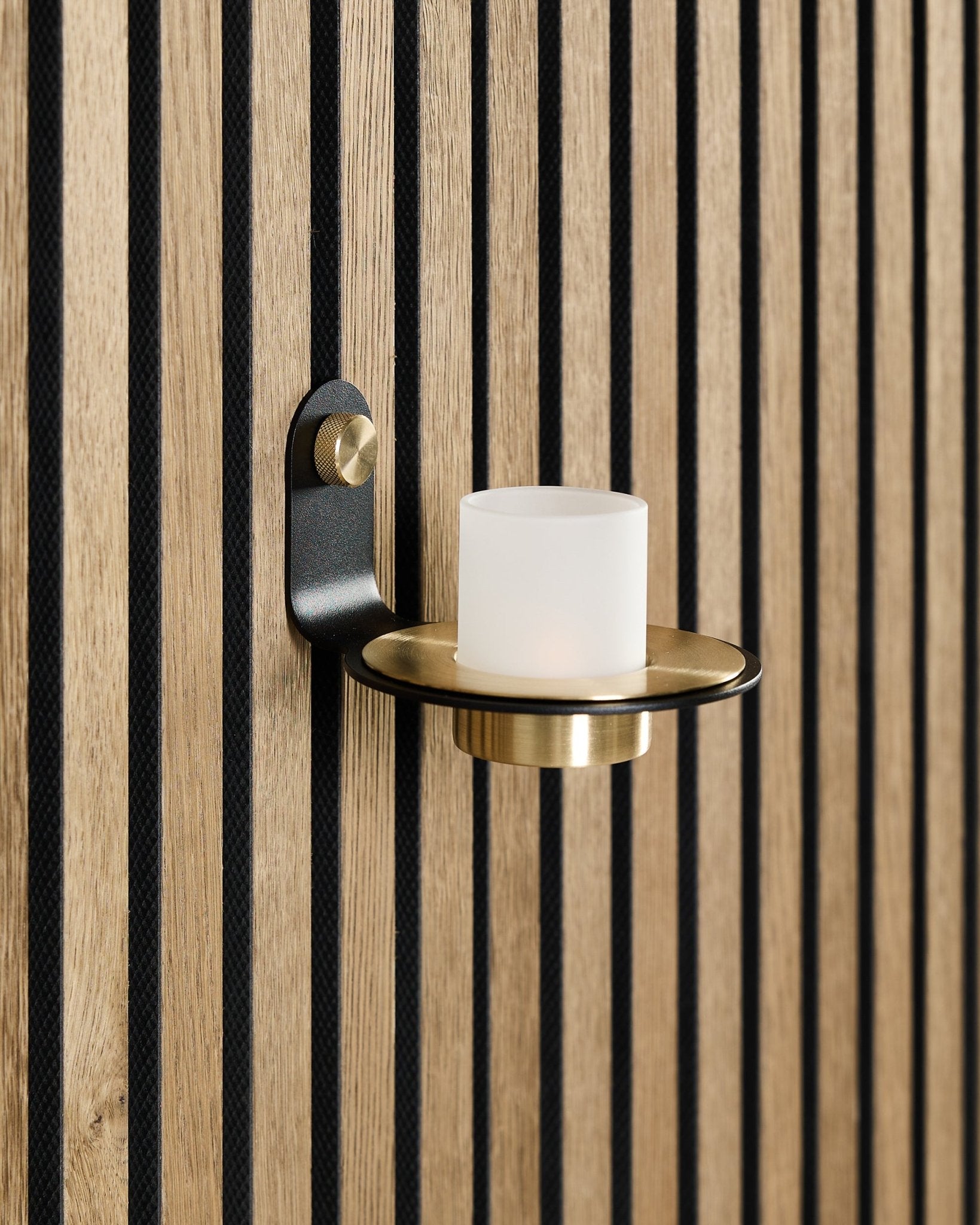 Der Norr Kerzenhalter in black und brass von WoodUpp ist auf einem nordischen Akupanel Akustikholzpaneel mit verticalen blacken Lamellen montiert.