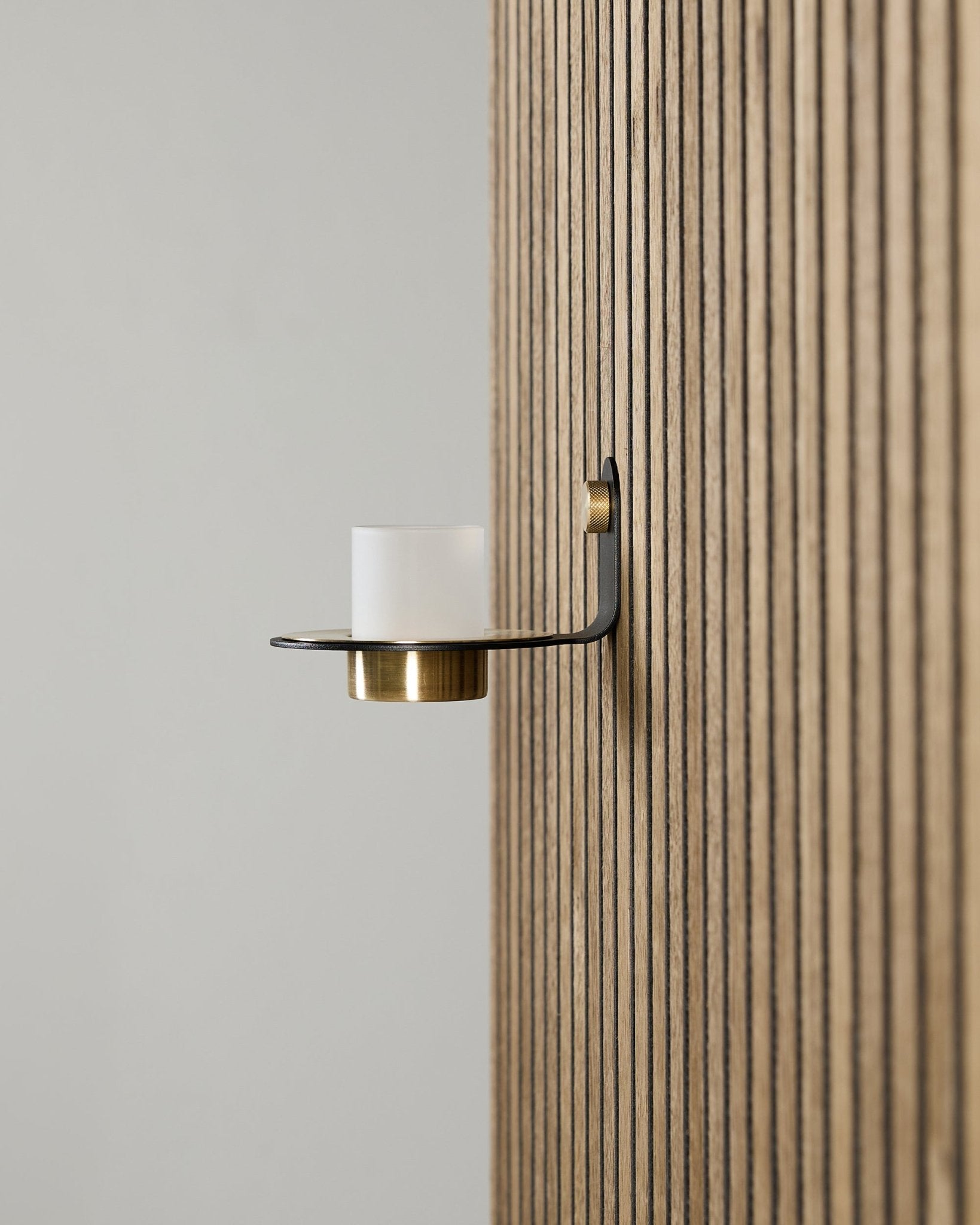 Norr Kerzenhalter in black und brass von WoodUpp, montiert auf einem verticalen Akupanel Akustikpaneel, mit satiniertem Glas und Details in brass.