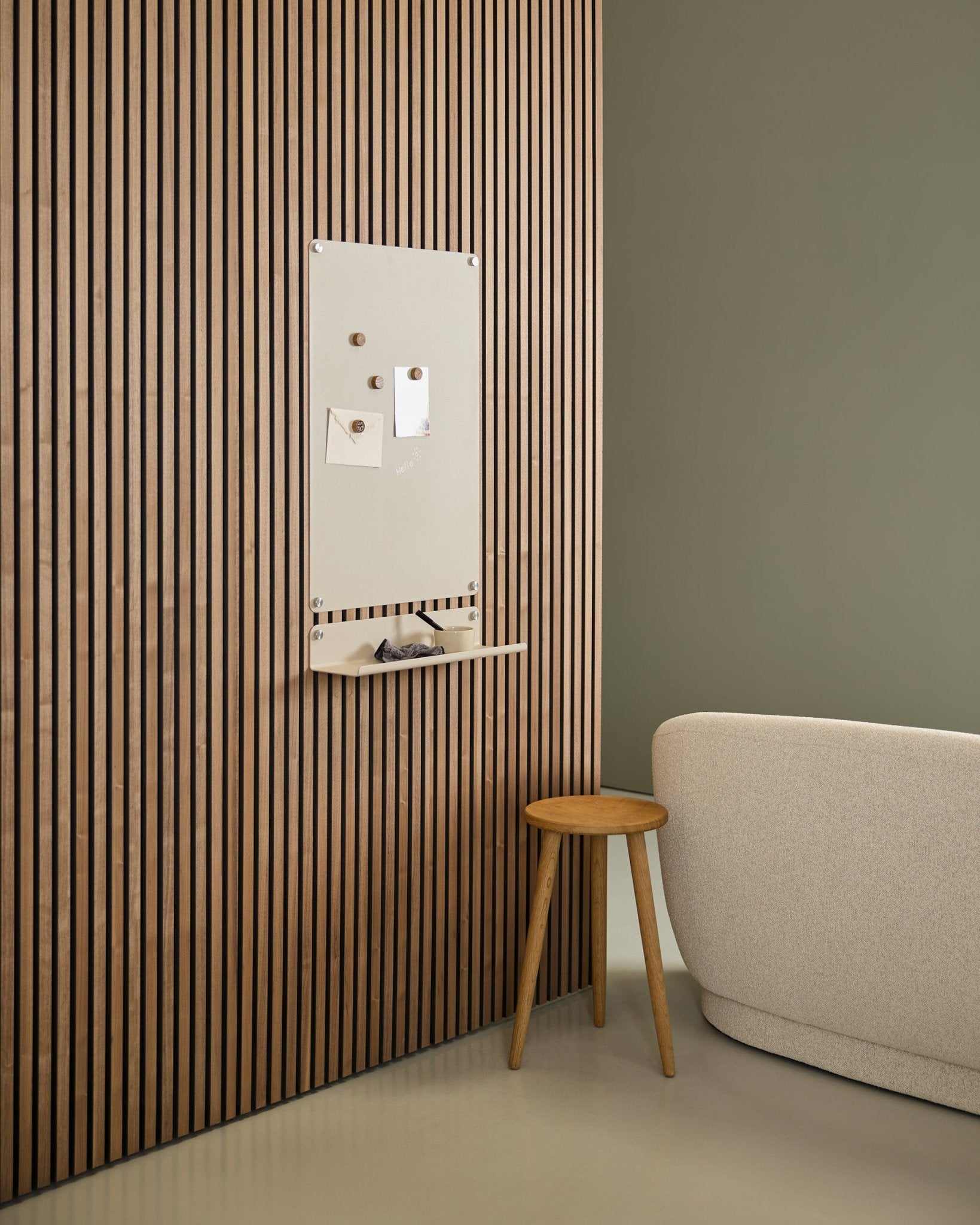 Minimalistisches Interieur mit beige Sofa und Holzschemel, mit einem WoodUpp large beige Norr Magnetic Board, montiert auf einem nordischen Akupanel Akustik-Holzpaneel neben einer grünen Wand.
