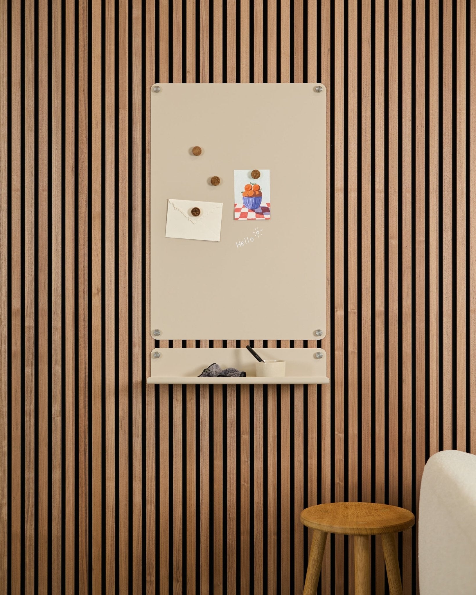 Beige Norr Magnetic Board von WoodUpp, montiert über einem small Regal an einer Wand aus Akupanel Akustik-Holzpaneelen, mit einem Schemel und einem weißen Sofa in der Nähe.