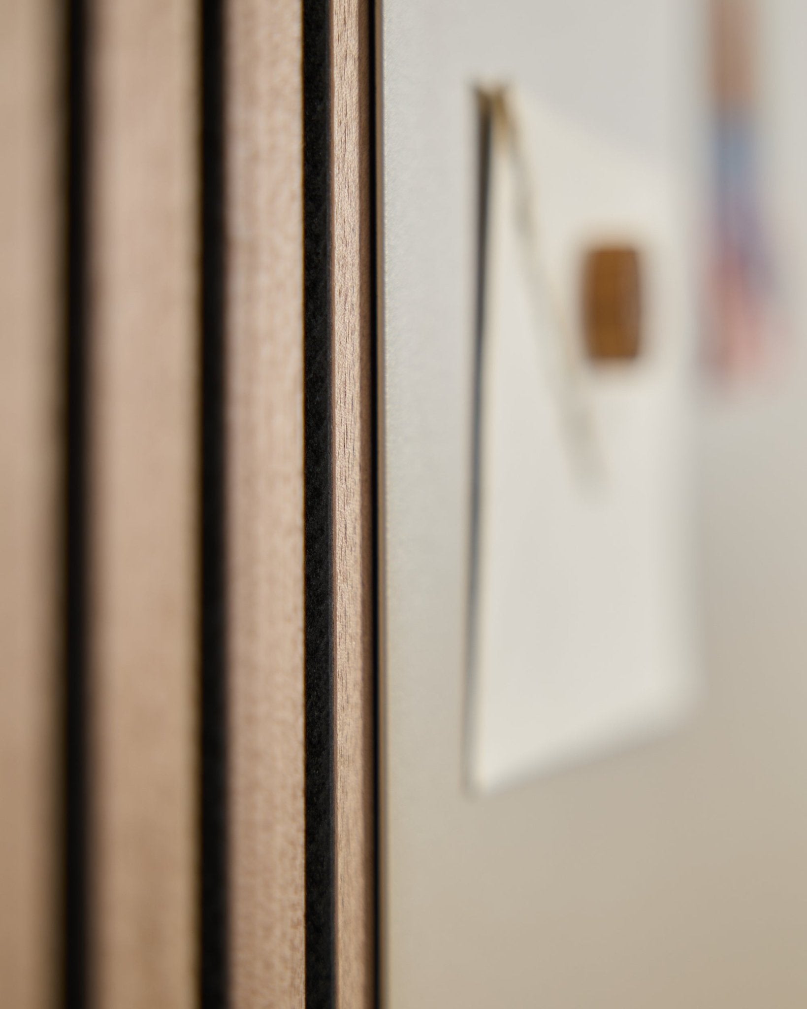 Nahaufnahme eines WoodUpp Akupanel Akustik-Holzpaneels mit vertical Lamellen, daneben im Hintergrund ein unscharfes large beige Norr Magnetic Board.