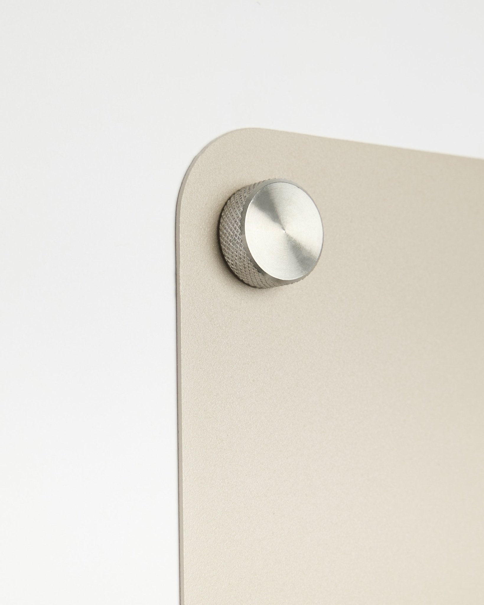 Nahaufnahme eines runden Metallknaufs als Zubehör, befestigt am large beige Norr Magnetic Board von WoodUpp, mit einem Detail aus satiniertem Glas vor weißem Hintergrund.