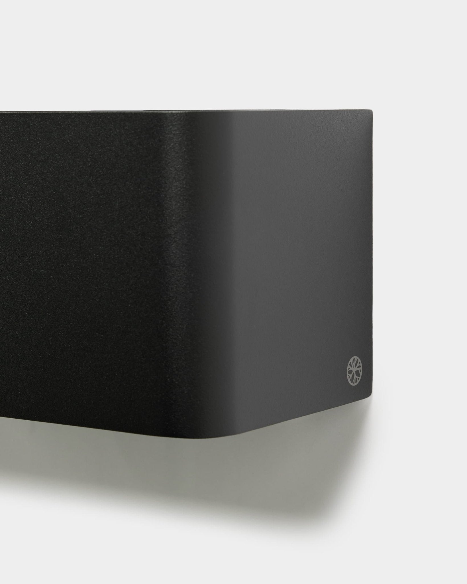 Gros plan sur la WoodUpp Norr Plant Box minimaliste (23,9 cm, black) aux bords arrondis et avec logo, fixée sur un mur blanc. Un accessoire acoustique au design nordique.