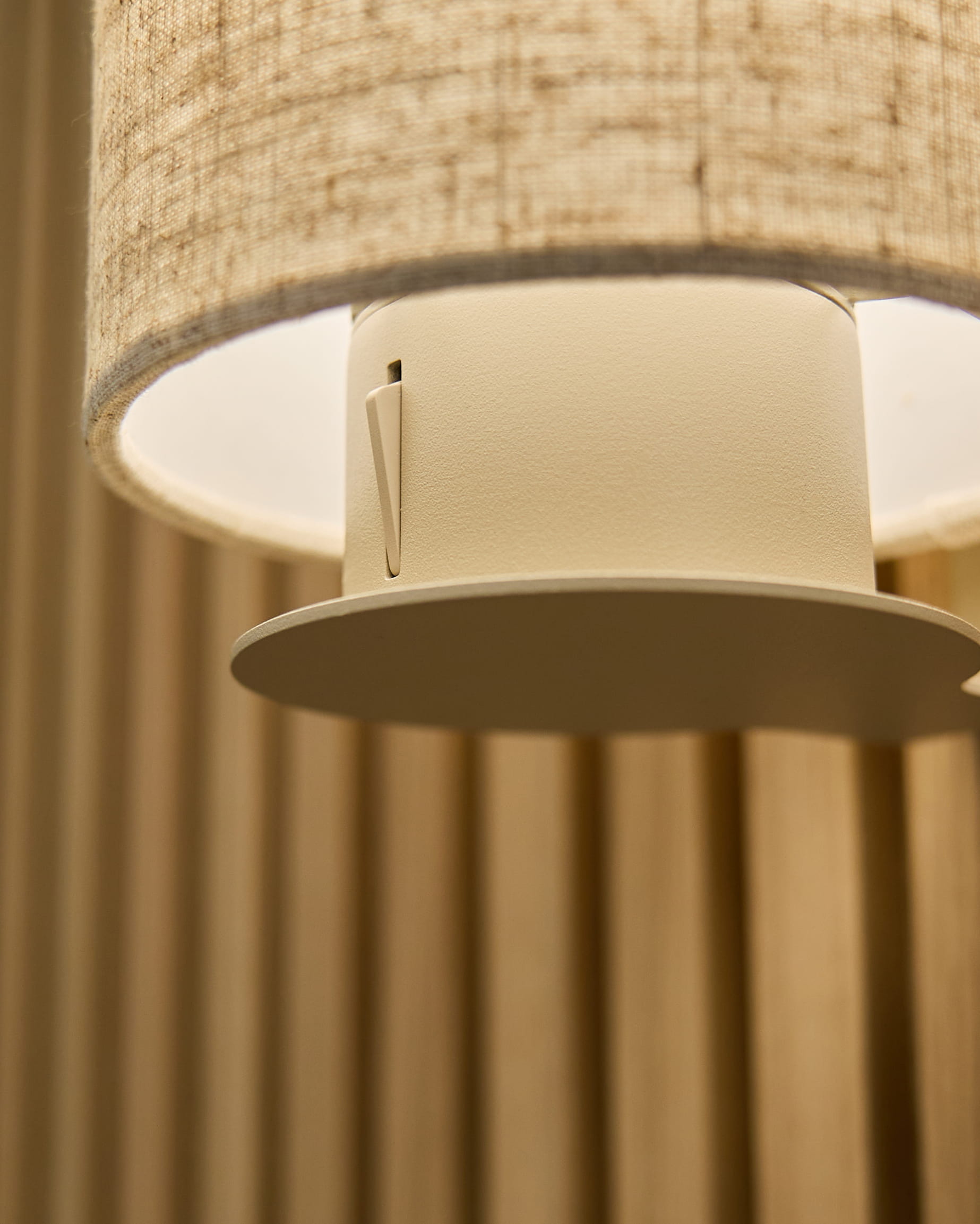 Gros plan sur la lampe murale Feya en Beige/Beige de WoodUpp, avec un abat-jour en lin-coton et un support cylindrique monté sur des panneaux acoustiques vertical beige.