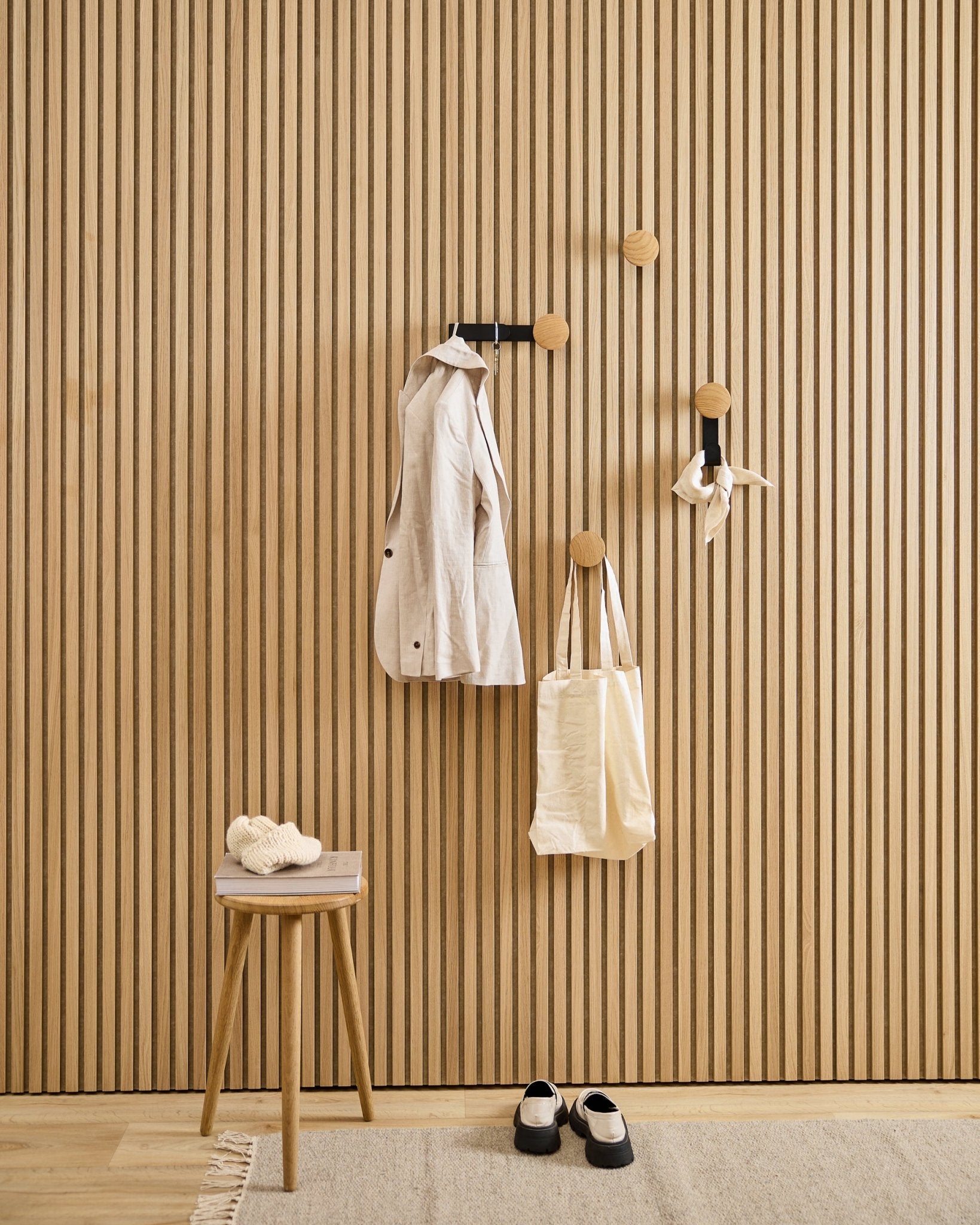 Minimalistischer Eingangsbereich mit dem WoodUpp Linn Vertical Hanger in natural oak, mit einem beigefarbenen Mantel, einer Tragetasche, einem Schal, einem Hocker mit Hausschuhen und black-weißen Schuhen.