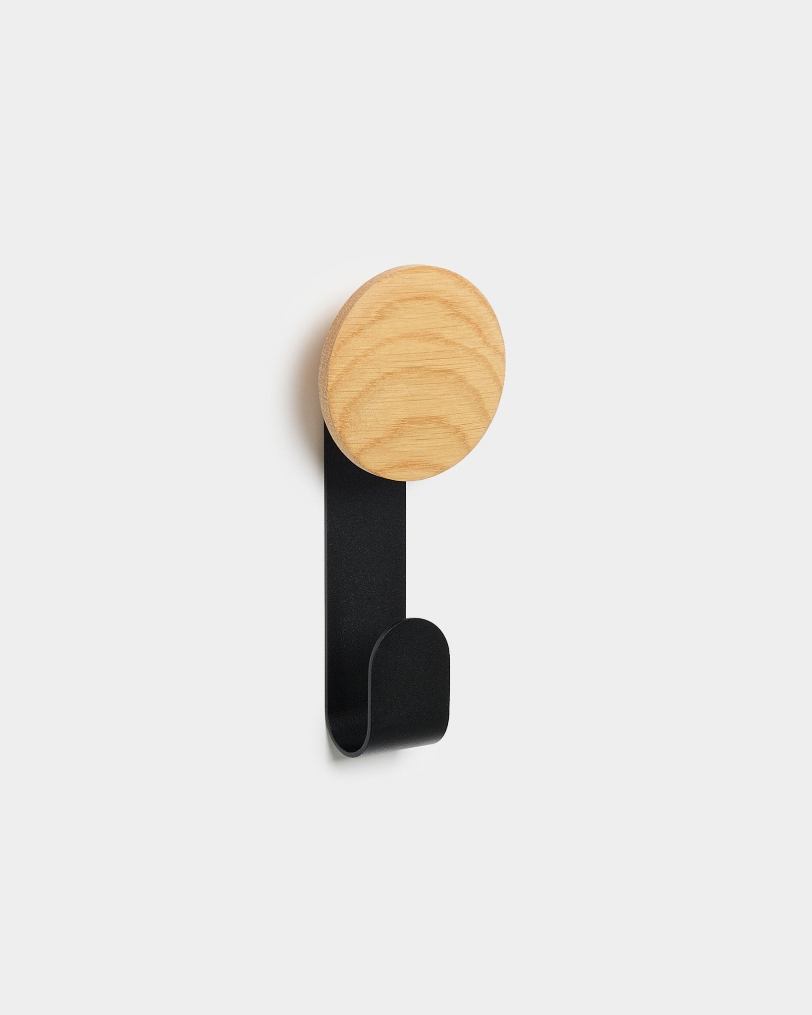 Der Linn Vertical Hanger von WoodUpp mit runder Oberseite aus natural oak und Haken aus black Metall wurde dafür entworfen, Accessoires an Akupanels Nordic Akustik-Holzpaneelen aufzuhängen.