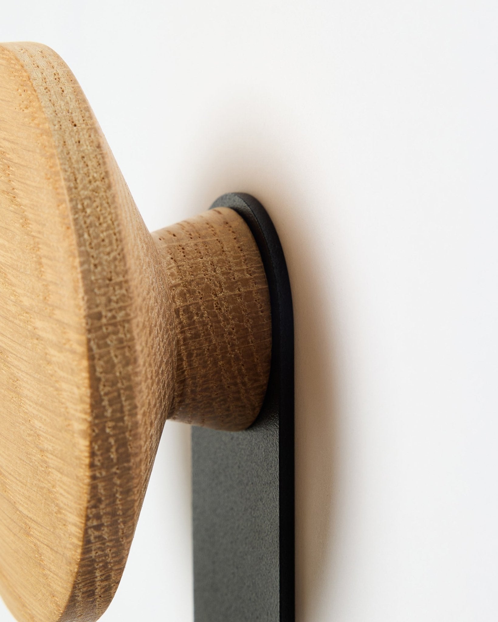 Nahaufnahme des Linn Vertical Hangers in natural oak von WoodUpp, ein rundes Holzknopf-Accessoire auf einer Halterung aus black, entworfen für Akupanel Akustikpaneele.