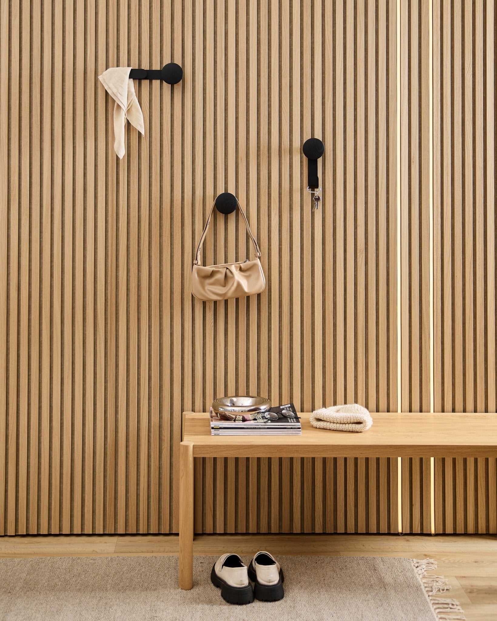 Minimalistischer Eingangsbereich mit einem WoodUpp Linn Horizontal Hanger in Black Oak mit blacken Haken, Holzbank, Schuhen, Büchern und einer Schale. Nordischer Stil.