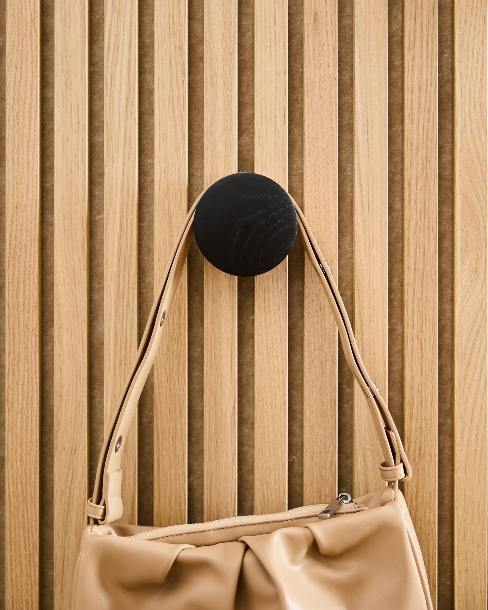Beige Handtasche an einem WoodUpp Linn | Single Hanger in Black Oak, montiert auf einem hellen Akupanel Akustik-Lamellenpaneel aus Holz.