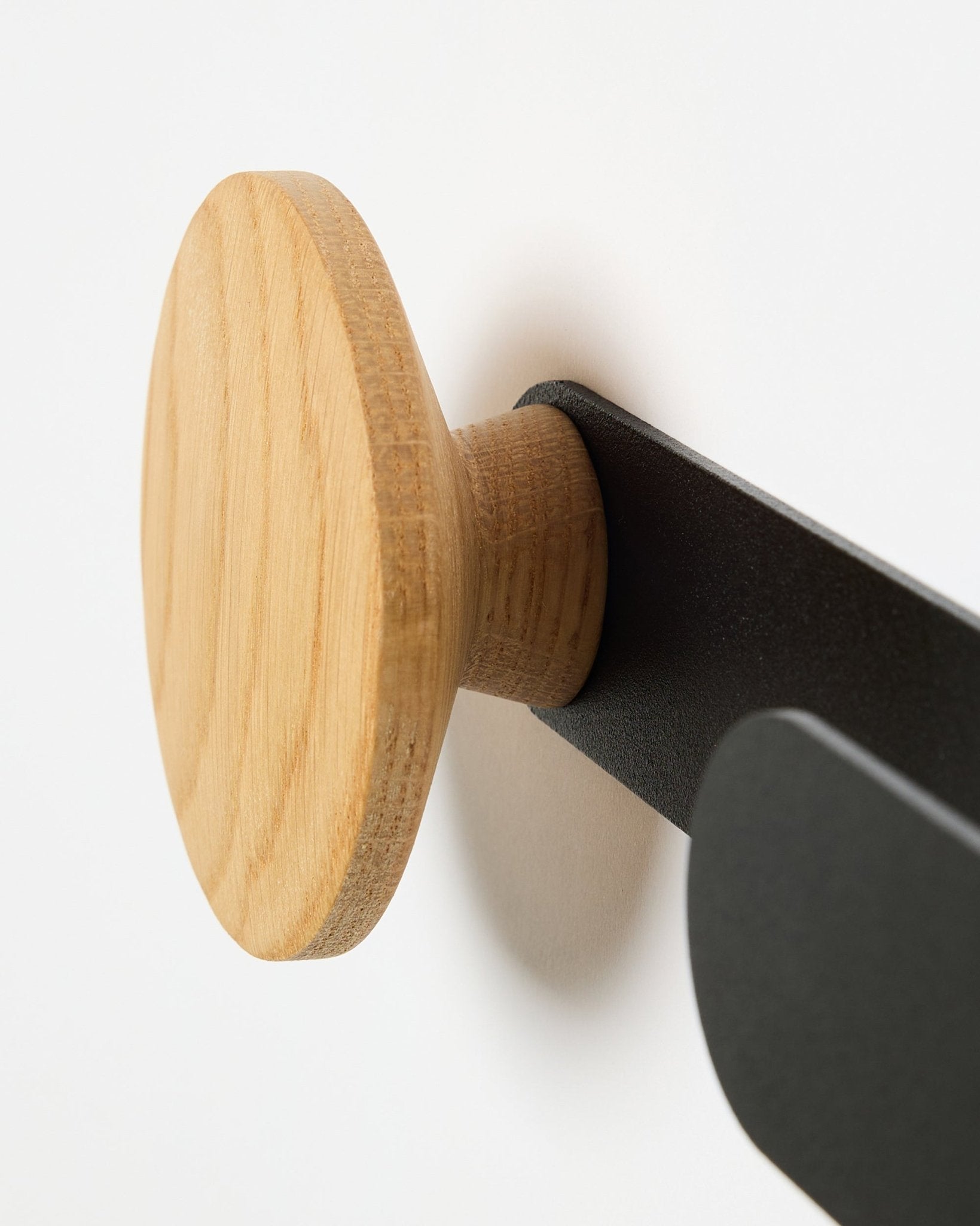 Nahaufnahme des WoodUpp Linn Horizontal Hanger in natural oak auf einer Metallhalterung in black, entwickelt für Akupanel Akustikpaneele oder als funktionaler Wandhaken.