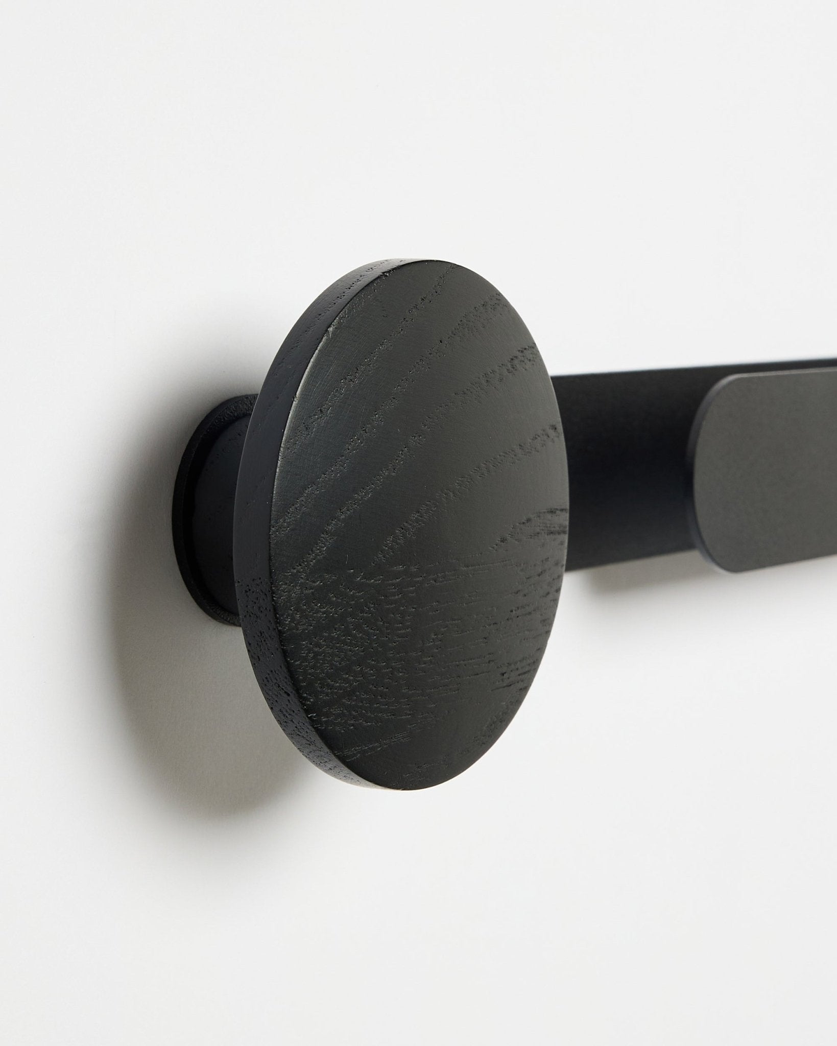 Nahaufnahme des WoodUpp Linn | Horizontal Hanger in Black Oak mit matter blacker Oberfläche, montiert an einer weißen Wand; Accessoire für Akustik-Holzpaneele.