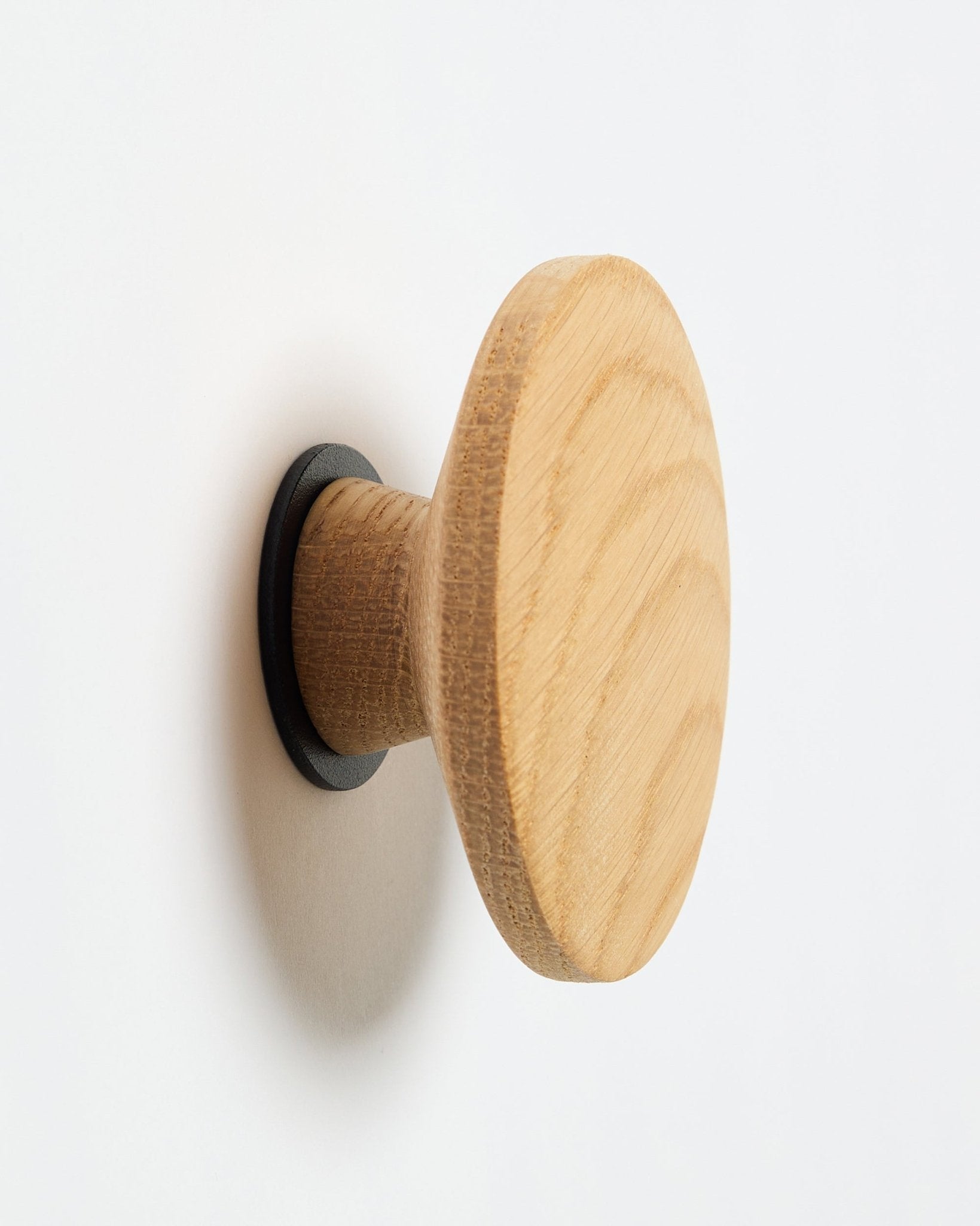 WoodUpp Linn I Single Hanger in natural oak, ein runder Wandhaken mit blacker Basis, entworfen als Zubehör zur Montage an Akupanel Akustikholzpaneelen.