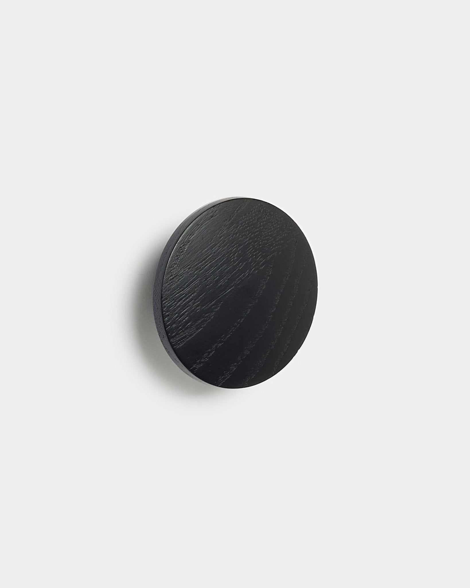 Der Linn | Single Hanger in black oak von WoodUpp, ein rundes Accessoire für Akupanel Akustikpaneele, ist vor einem schlichten weißen Hintergrund zu sehen.