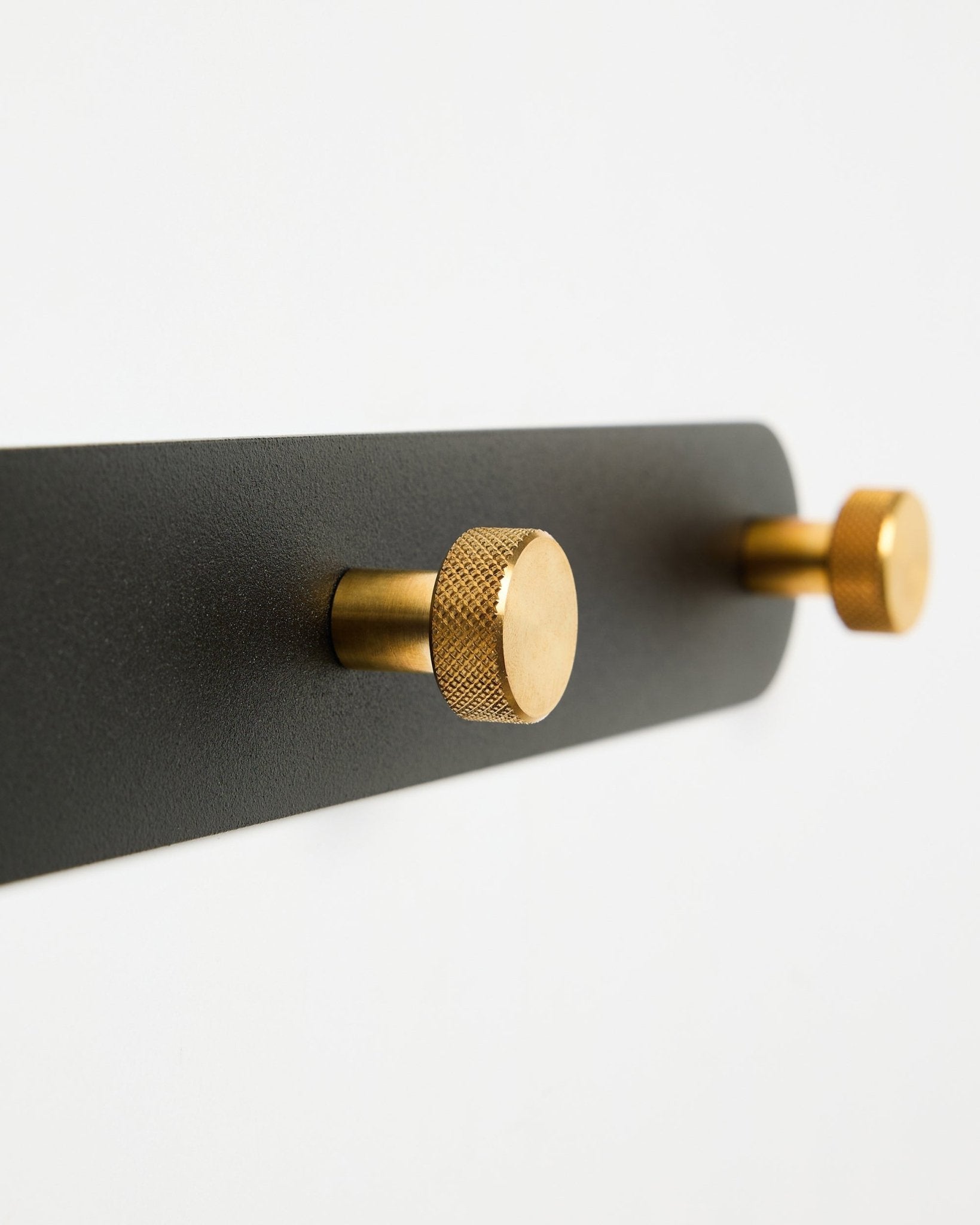 WoodUpp Norr Garderobenhakenleiste, Modell X7, mit zwei zylindrischen black und brass Haken auf einer black Halterung, dargestellt vor weißem Hintergrund.