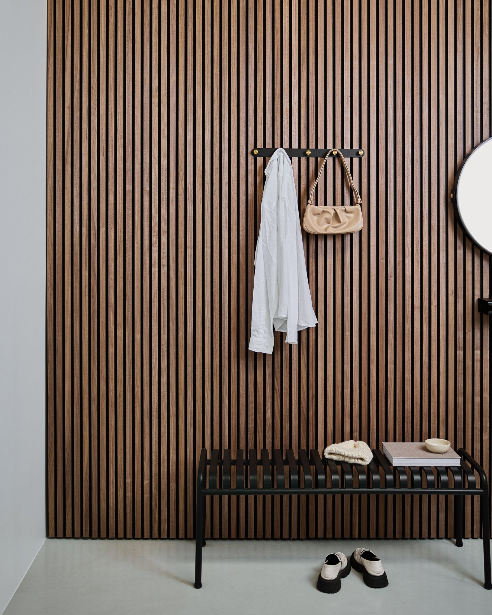 Le porte-manteau WoodUpp Norr en black et brass accueille une chemise blanche et un sac beige au-dessus d’un banc black ; des chaussons blancs sont soigneusement rangés en dessous.
