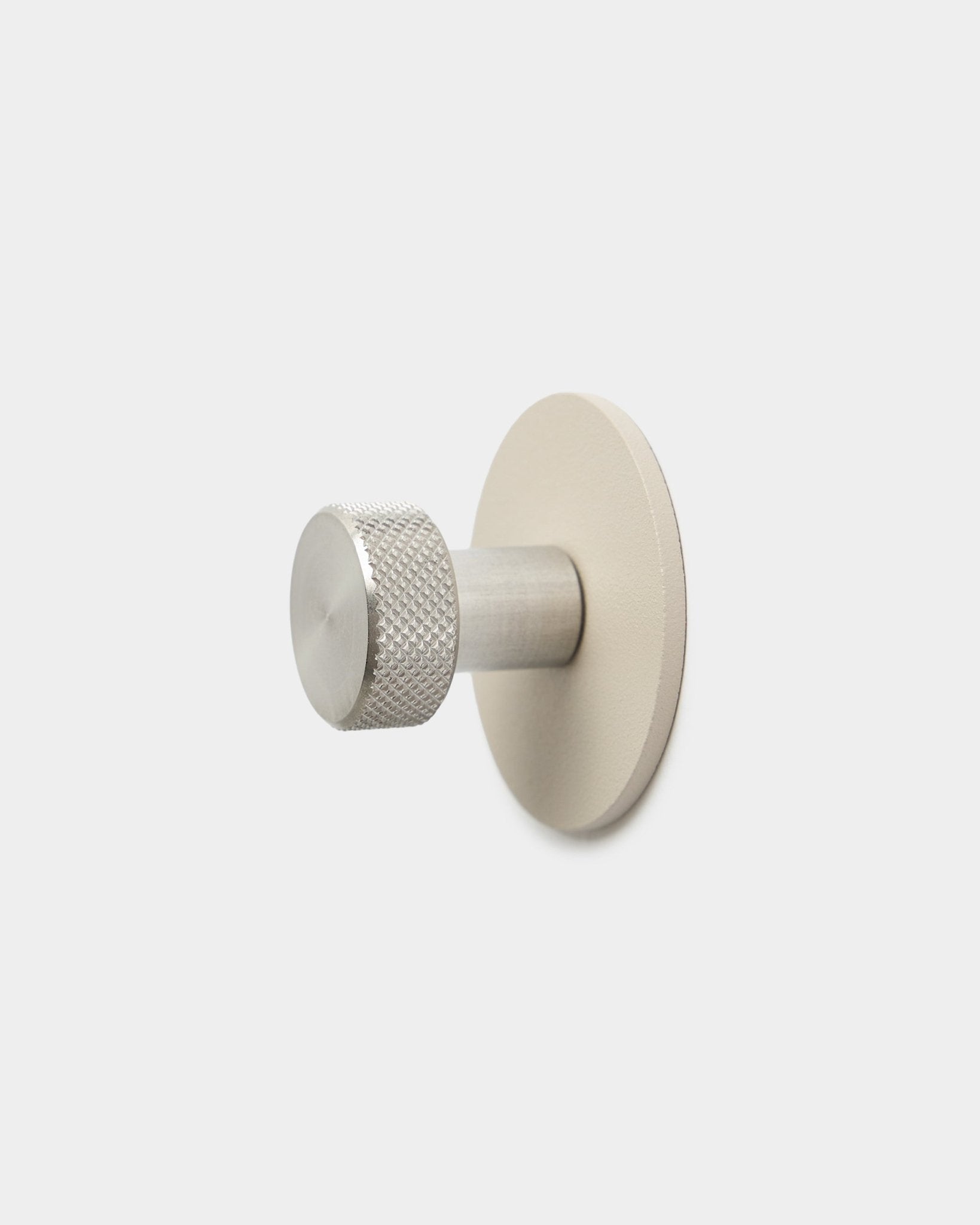 Patère WoodUpp Norr en beige et steel inoxydable, avec une extrémité cylindrique texturée et une base ronde, accessoire pour Akupanel, sur fond blanc uni.