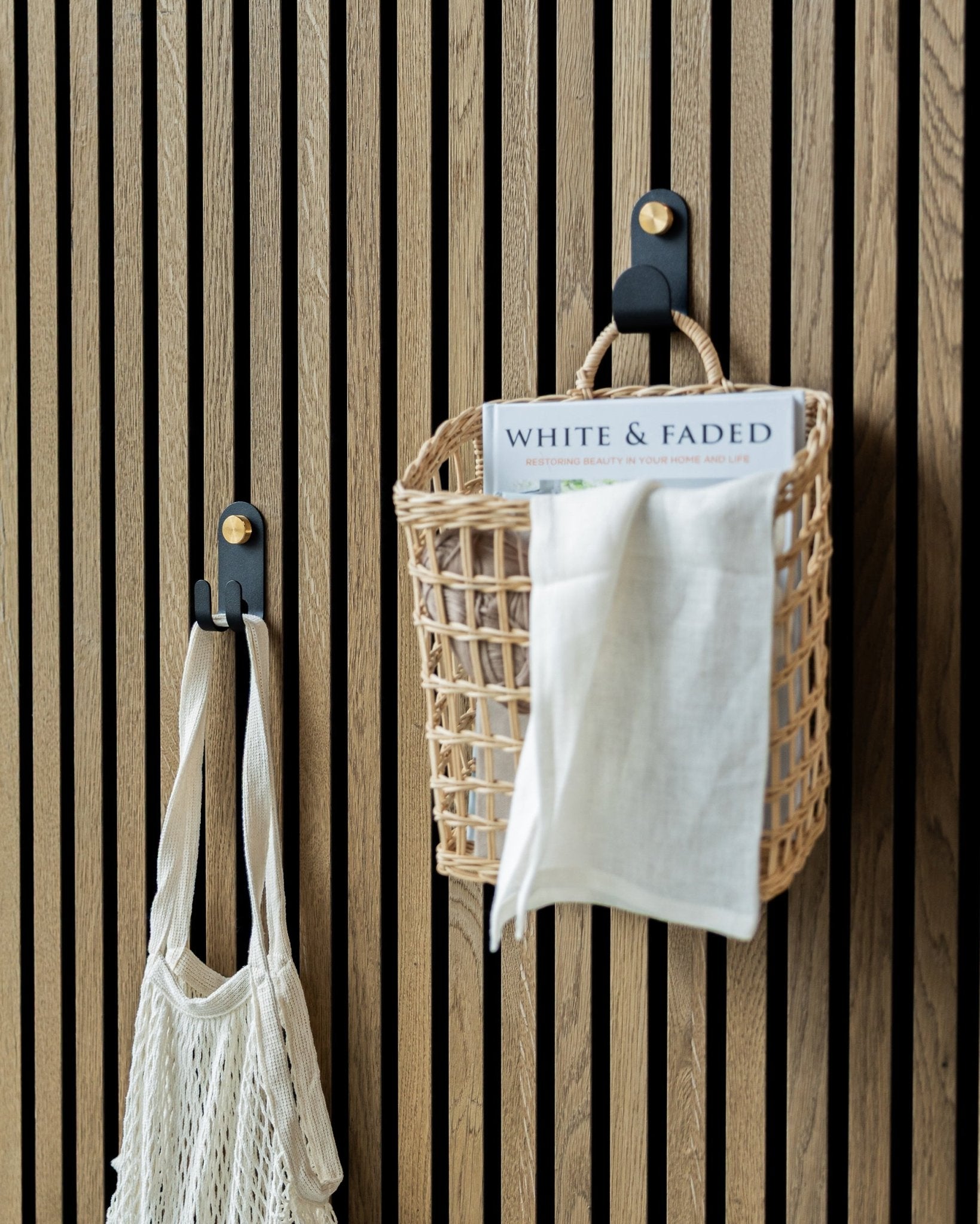Le Norr Single Hanger de WoodUpp en Black supporte un panier tressé et un sac en filet, montés sur un panneau acoustique à lattes nordique pour un rangement bien organisé.