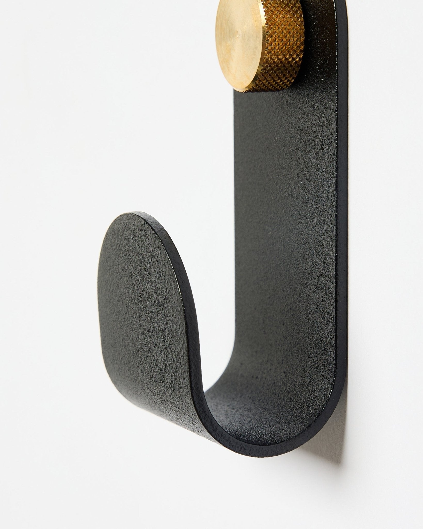 Le Norr Single Hanger de WoodUpp possède un bras courbé en métal black avec un embout doré, conçu comme accessoire à utiliser avec des panneaux acoustiques sur des murs blancs.