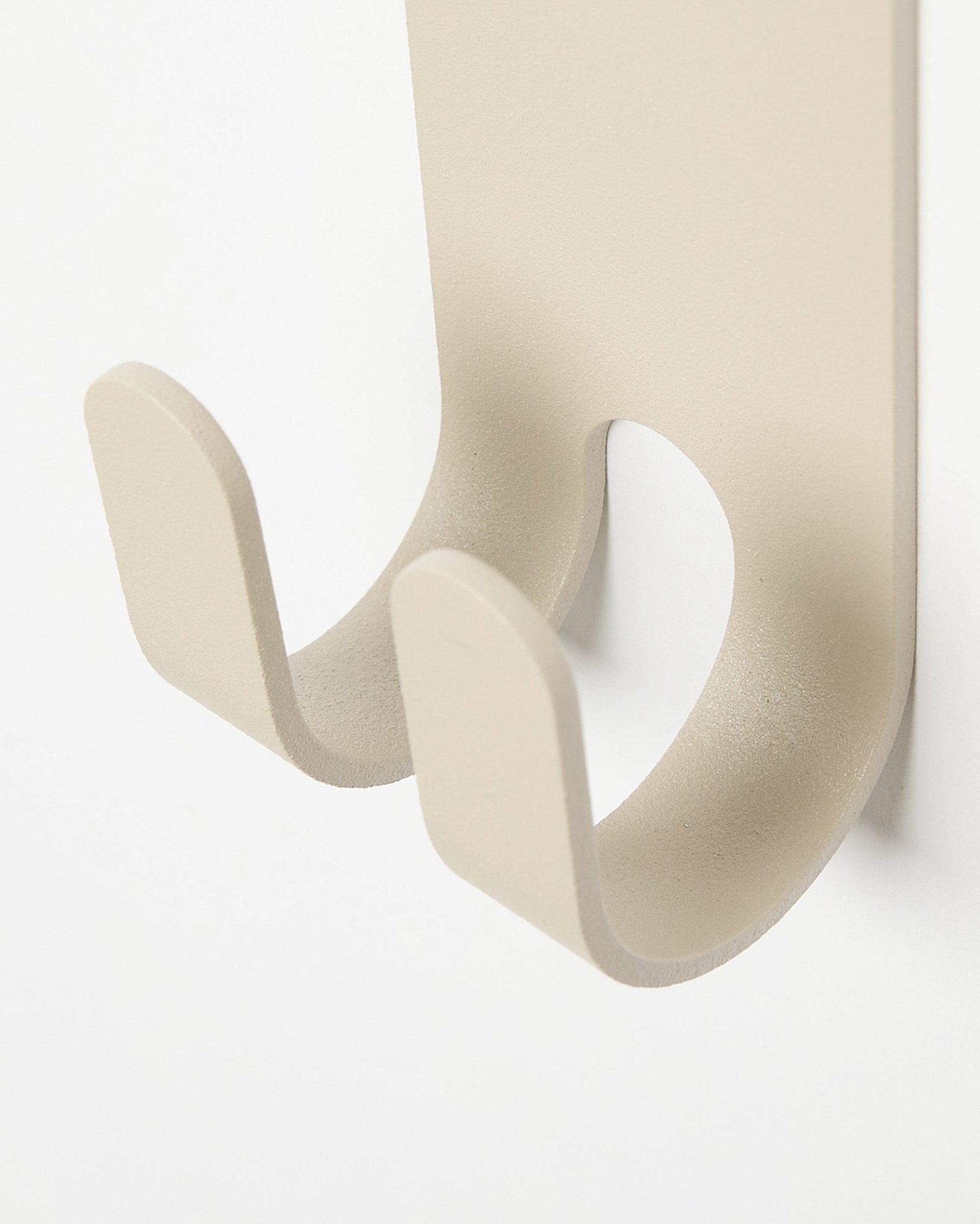 Nahaufnahme des Norr Double Hanger in beige von WoodUpp, ein minimalistischer Metallhaken, installiert auf einem hellen Akustikpaneel in colored.