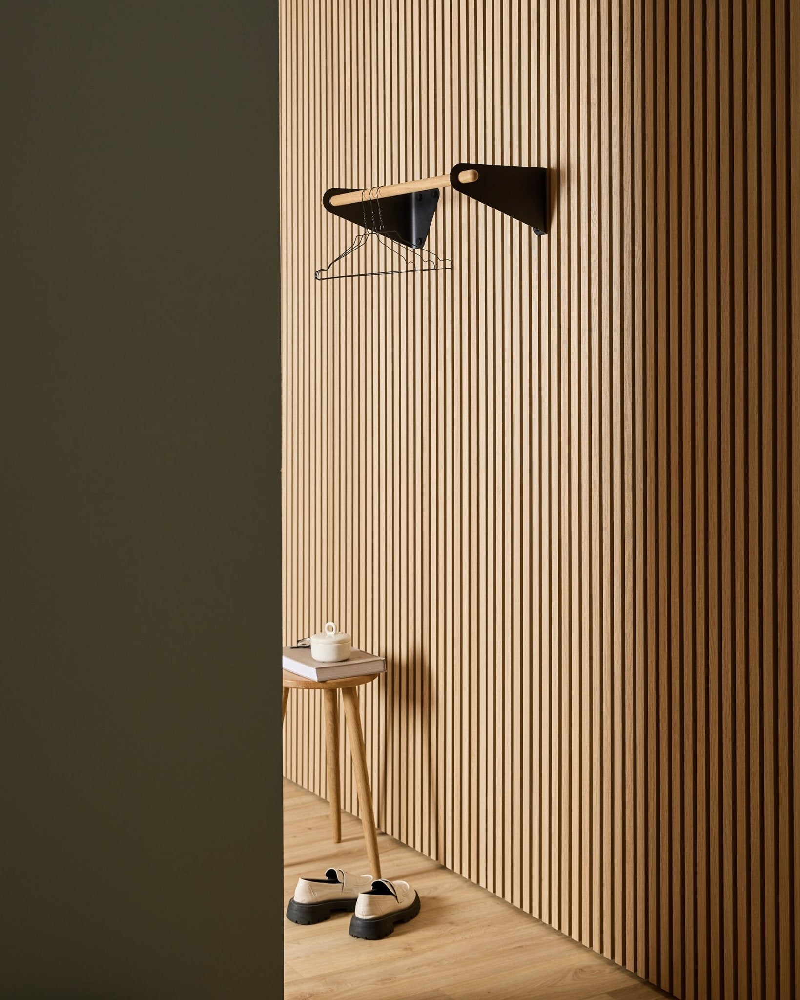 Minimalistischer Eingangsbereich mit WoodUpp Akupanel Nordic Akustik-Holzlamellenpaneelen, black Linn Garderobenleiste (75,9 cm), Hocker, Schuhen, Wandregal und Papierrolle.