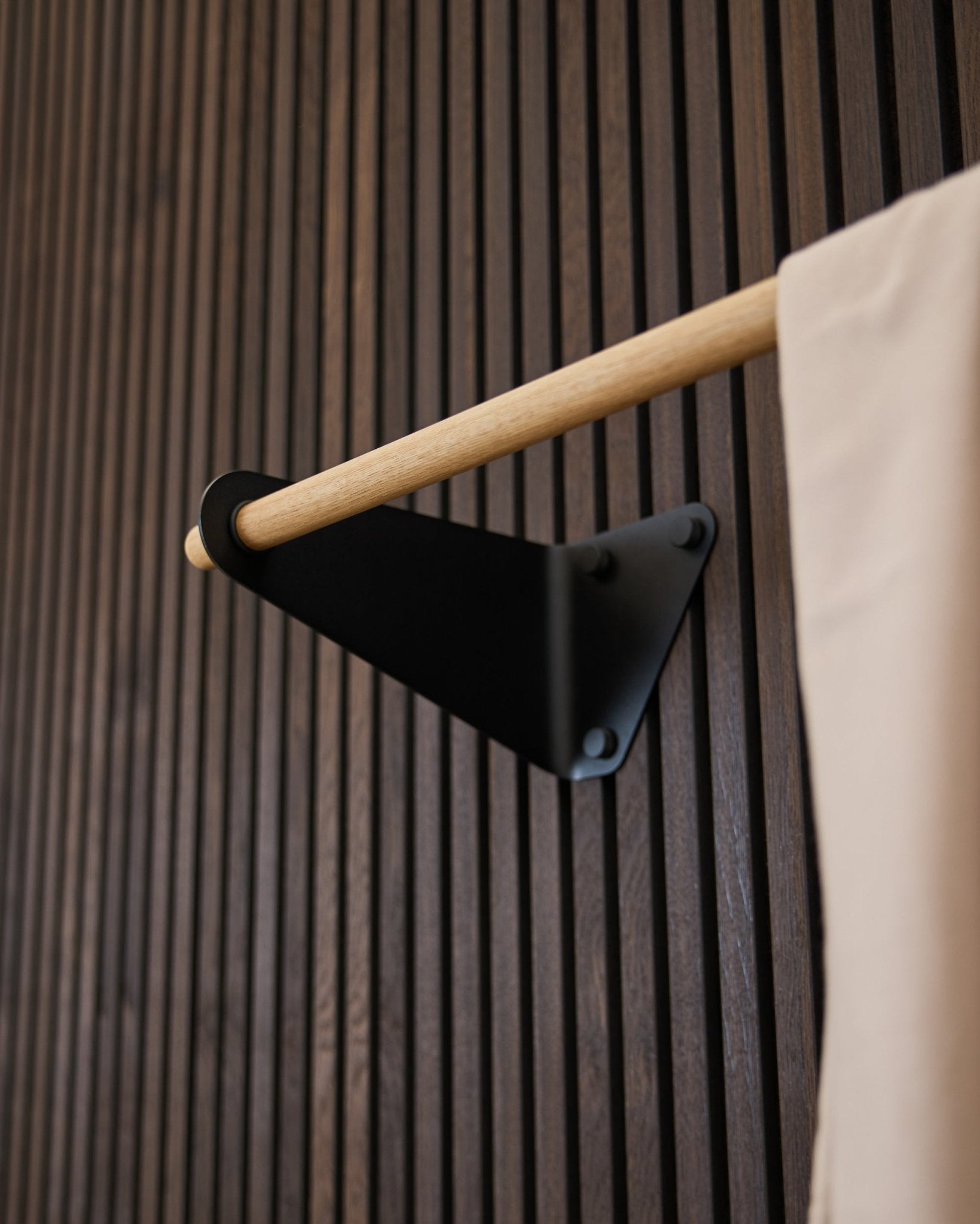 Linn Coat Rail von WoodUpp in black (115,9 cm), montiert auf einem dunklen gerillten Akupanel Akustikpaneel, mit beige Stoffakzent und black Halterung.